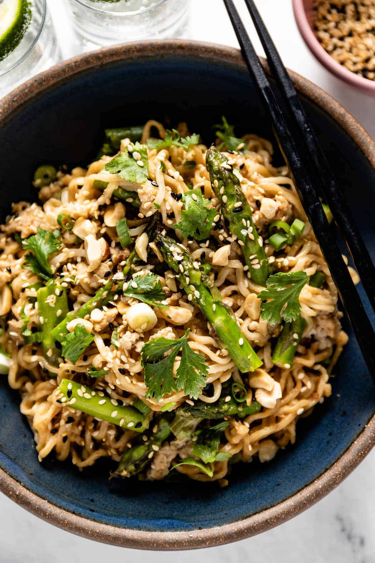 Sesame chicken noodles in a bowl garnished with peanuts and sesame seeds