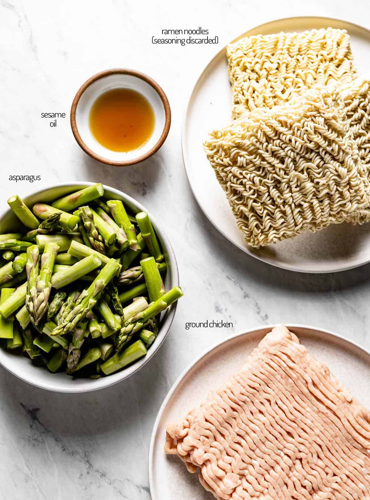 ingredients including asparagus, ramen noodles, and ground chicken on a marble backdrop