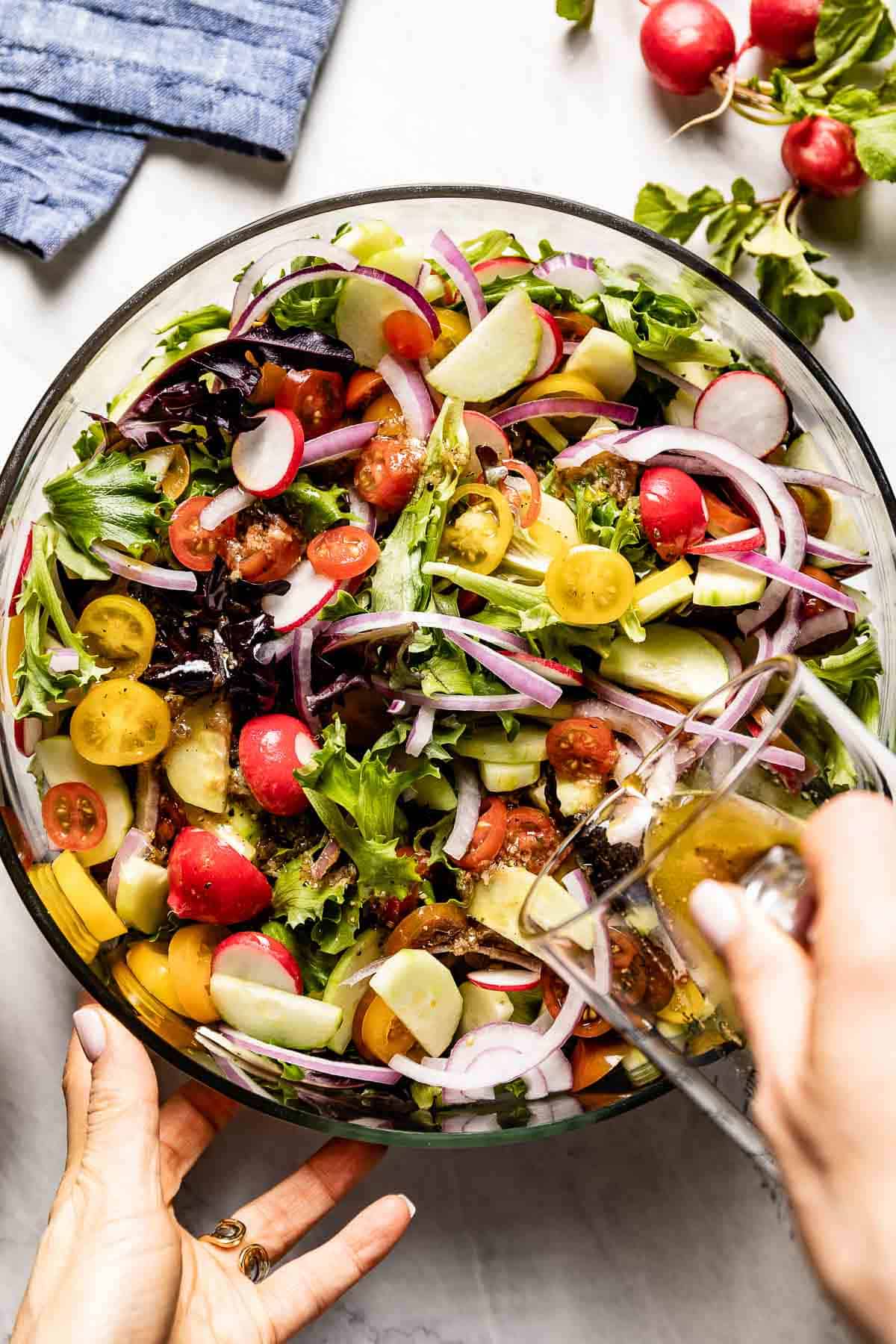 person drizzling a summer green salad with dressing