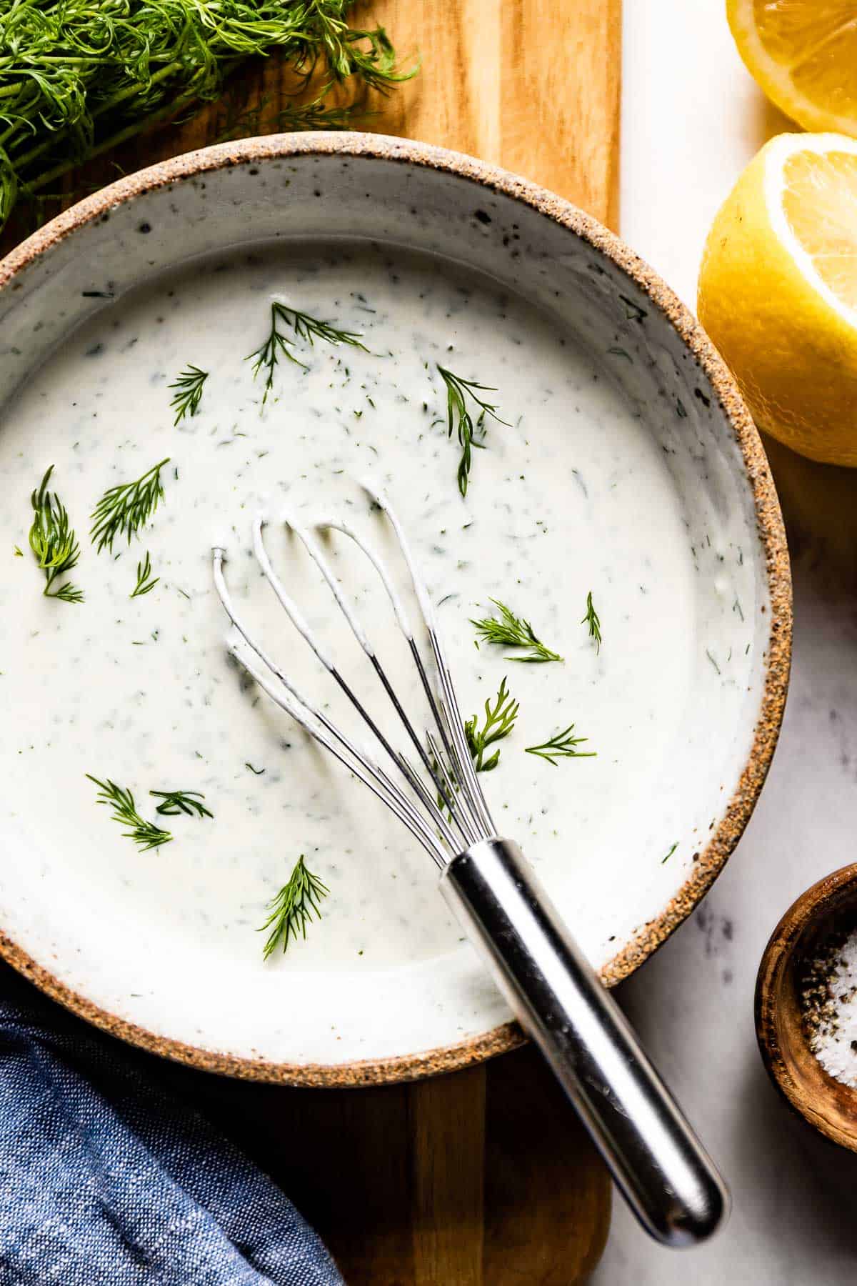 A bowl of dill yogurt sauce with a whisk in the bowl from the top view