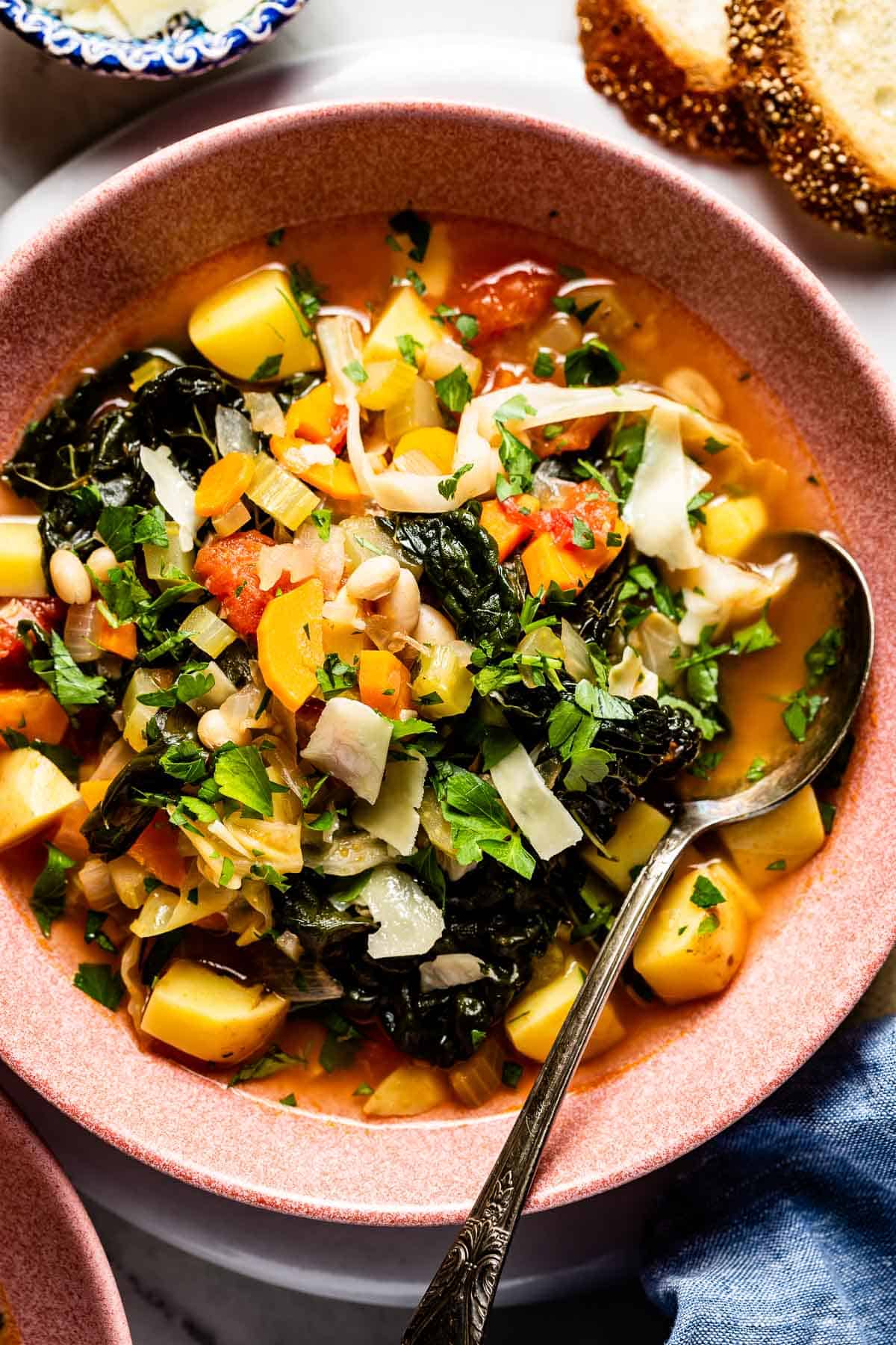 A bowl of soup with vegetables and kale with a spoon on the side from the top view. 