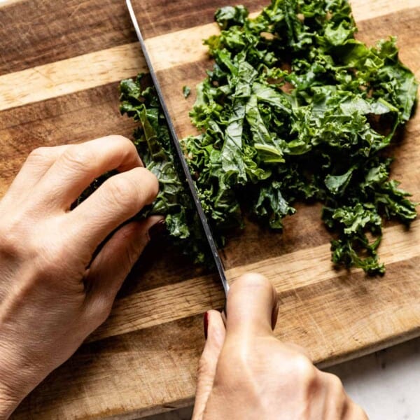 A person showing how to cut kale on a cutting board from the top view.