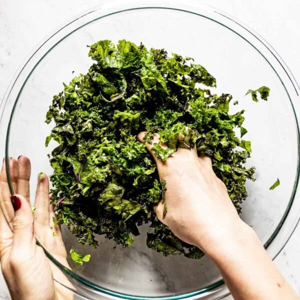 A person massaging kale in a bowl from the top view.