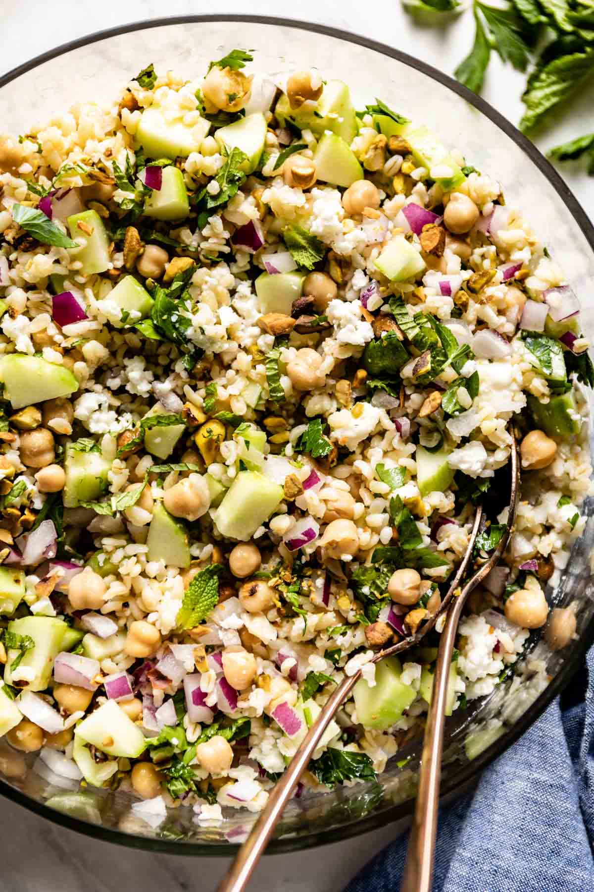 A salad with bulgur, veggies, herbs, cheese, and pistachios in a bowl from the top view. 