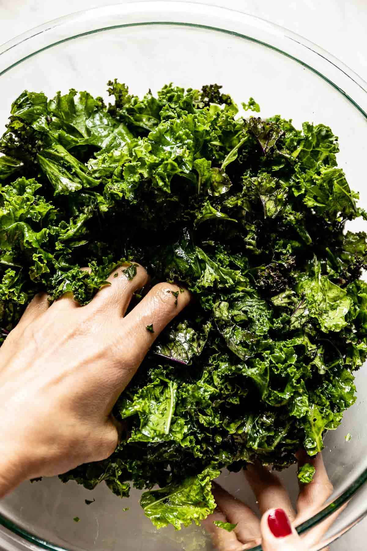 A person massaging kale with oil in a bowl from the top view.