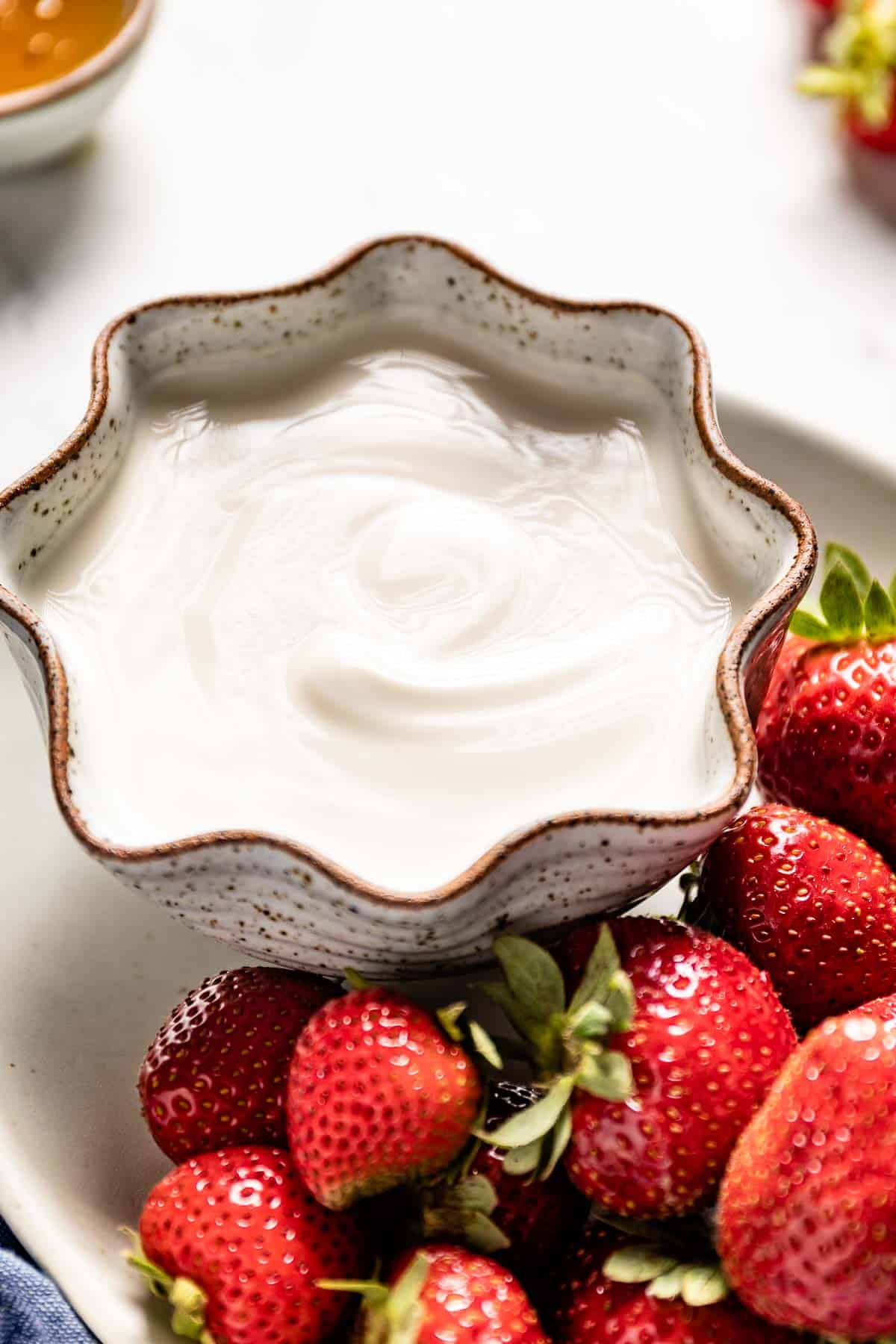 plain vanilla yogurt with honey in a bowl with strawberries on the side from the side view