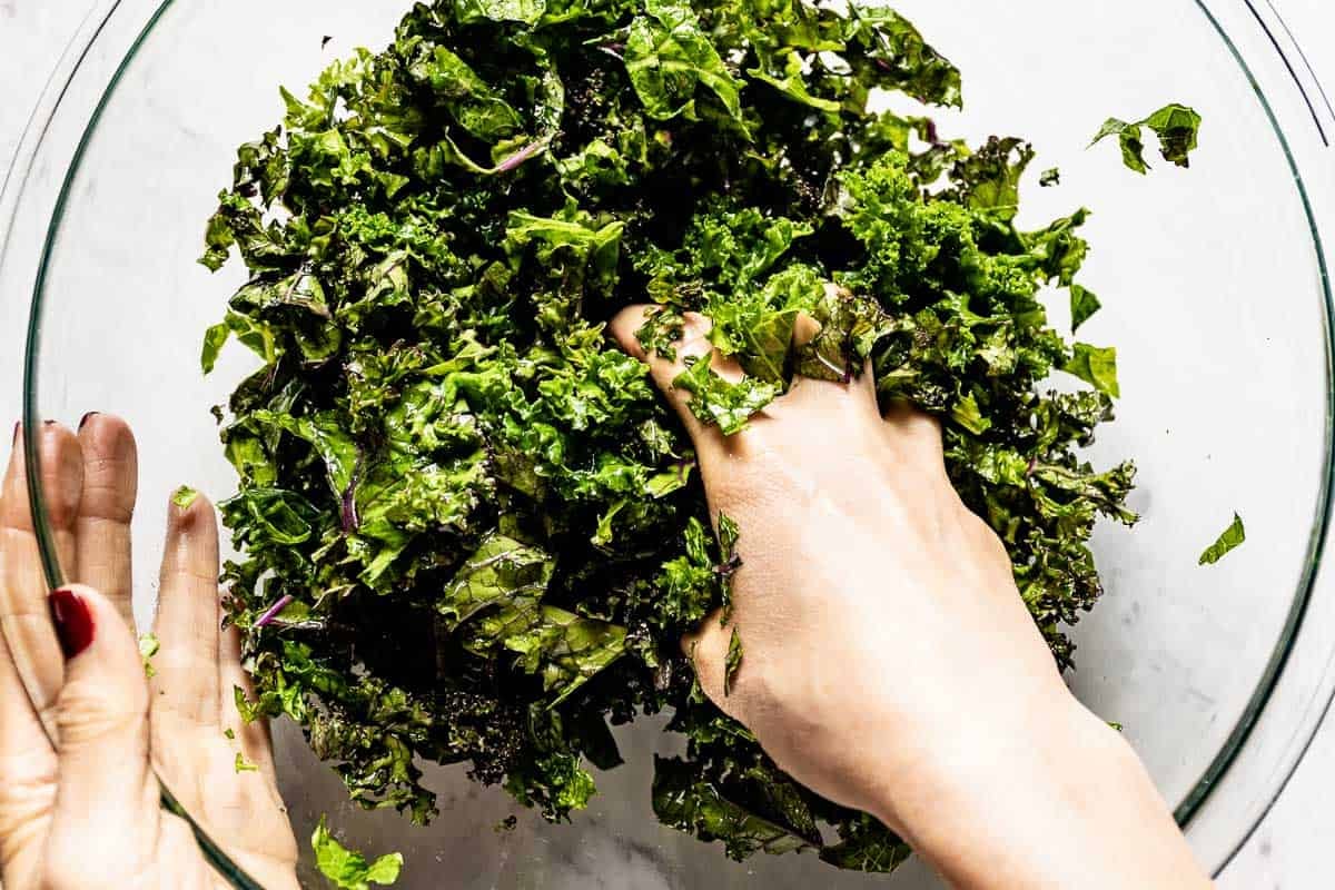 Hands massaging kale in a bowl until it softens and turns a vibrant dark green.