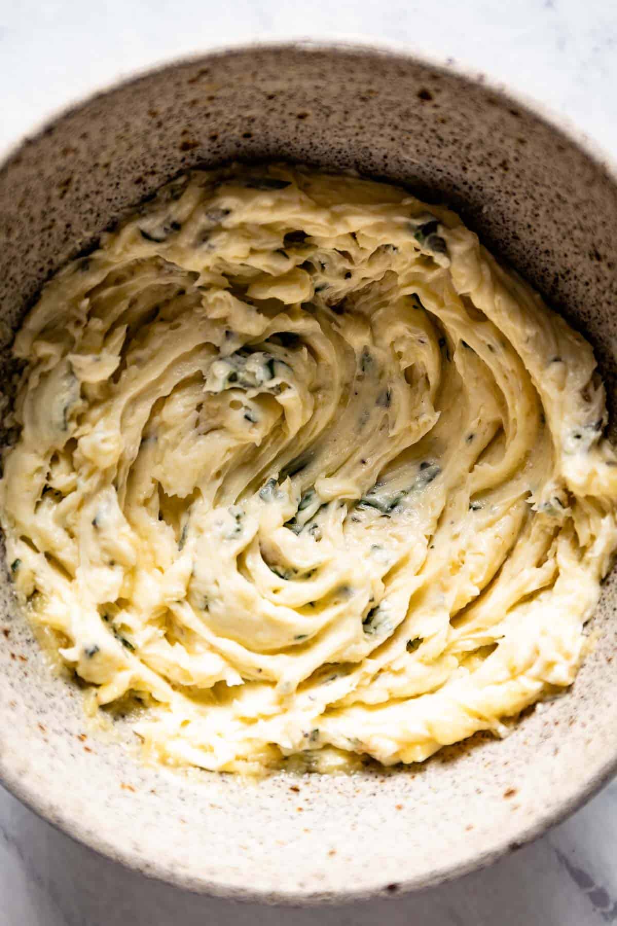 A bowl of compound butter with garlic and herbs from the top view.