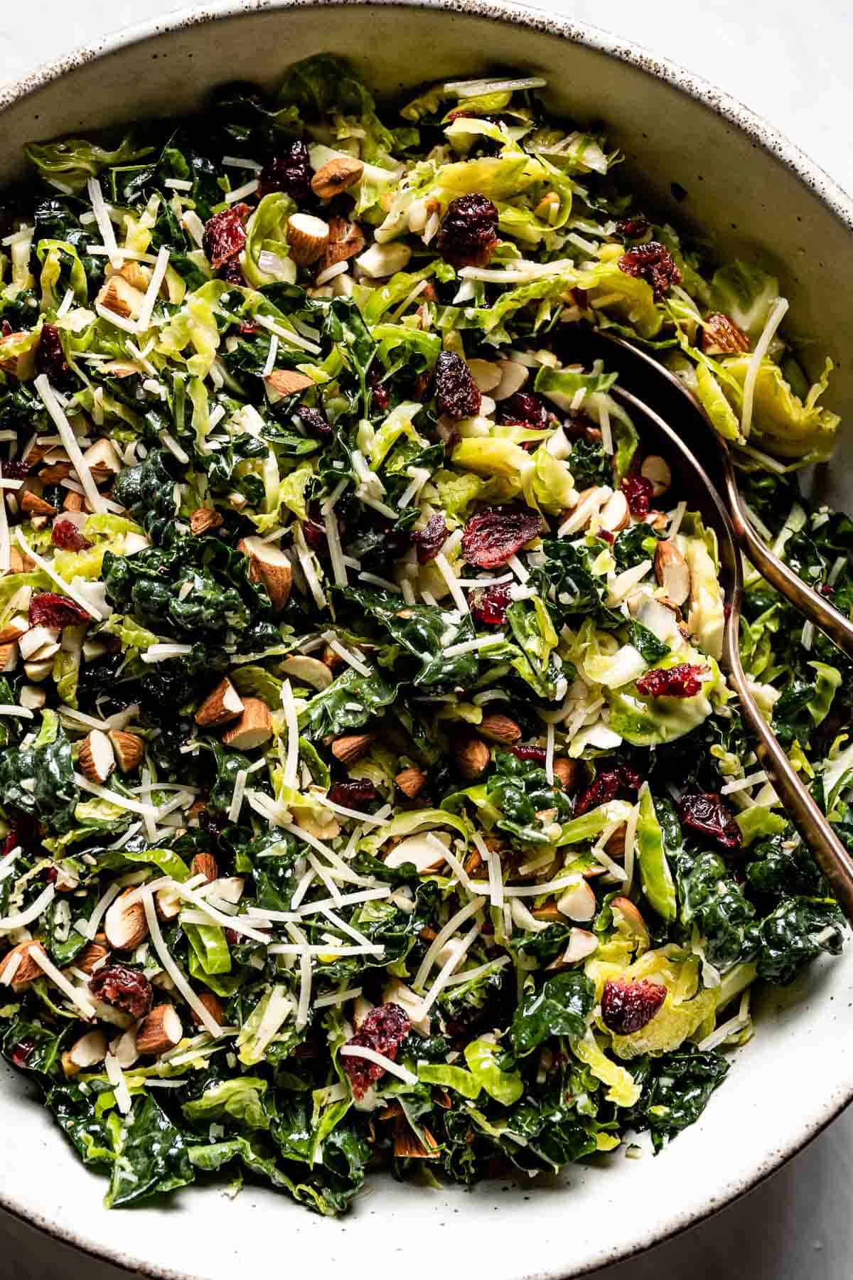 A kale Brussel sprout salad in a bowl with spoons from the top view. 
