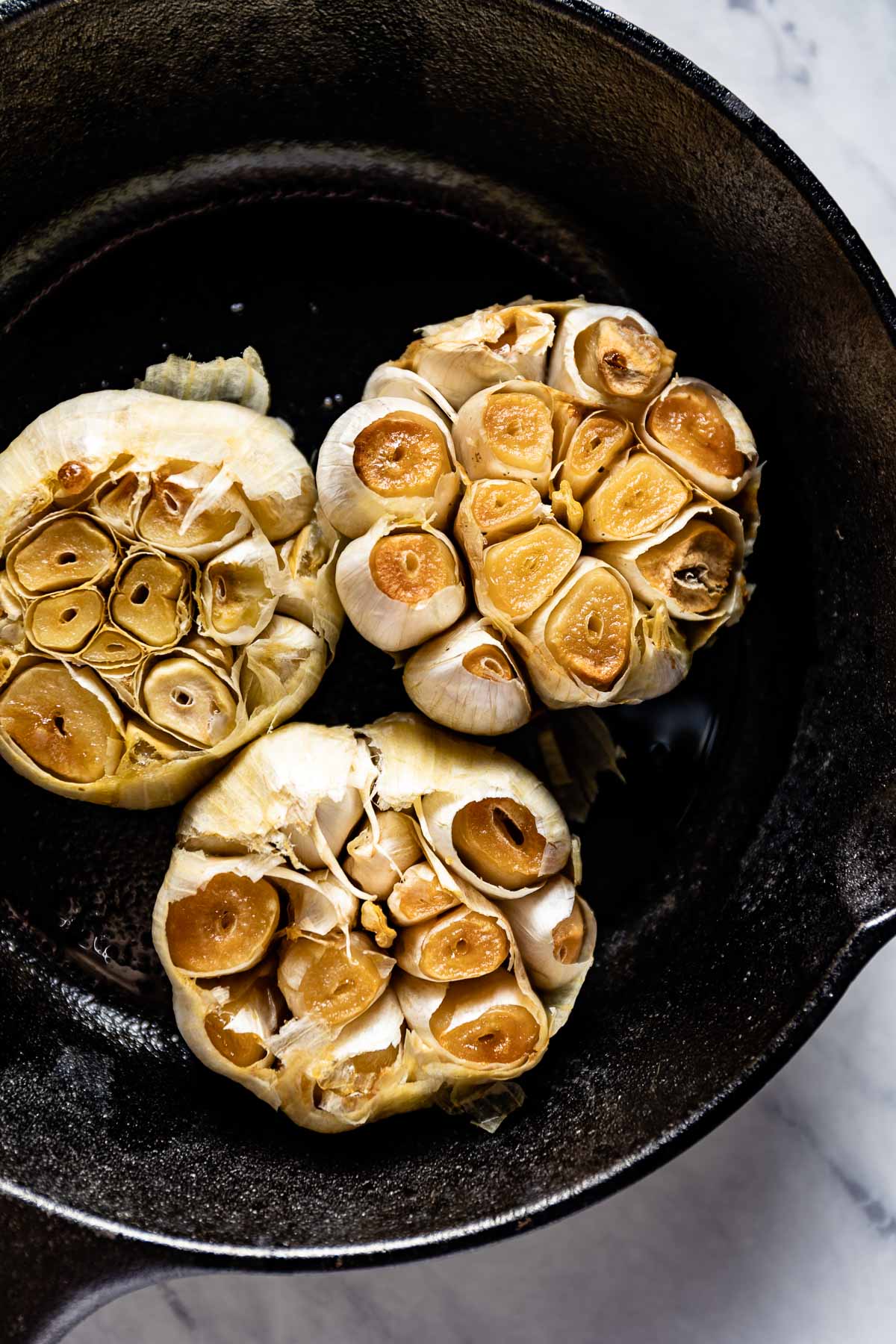 Heads of roasted garlic in a cast iron skillet from the top view. 