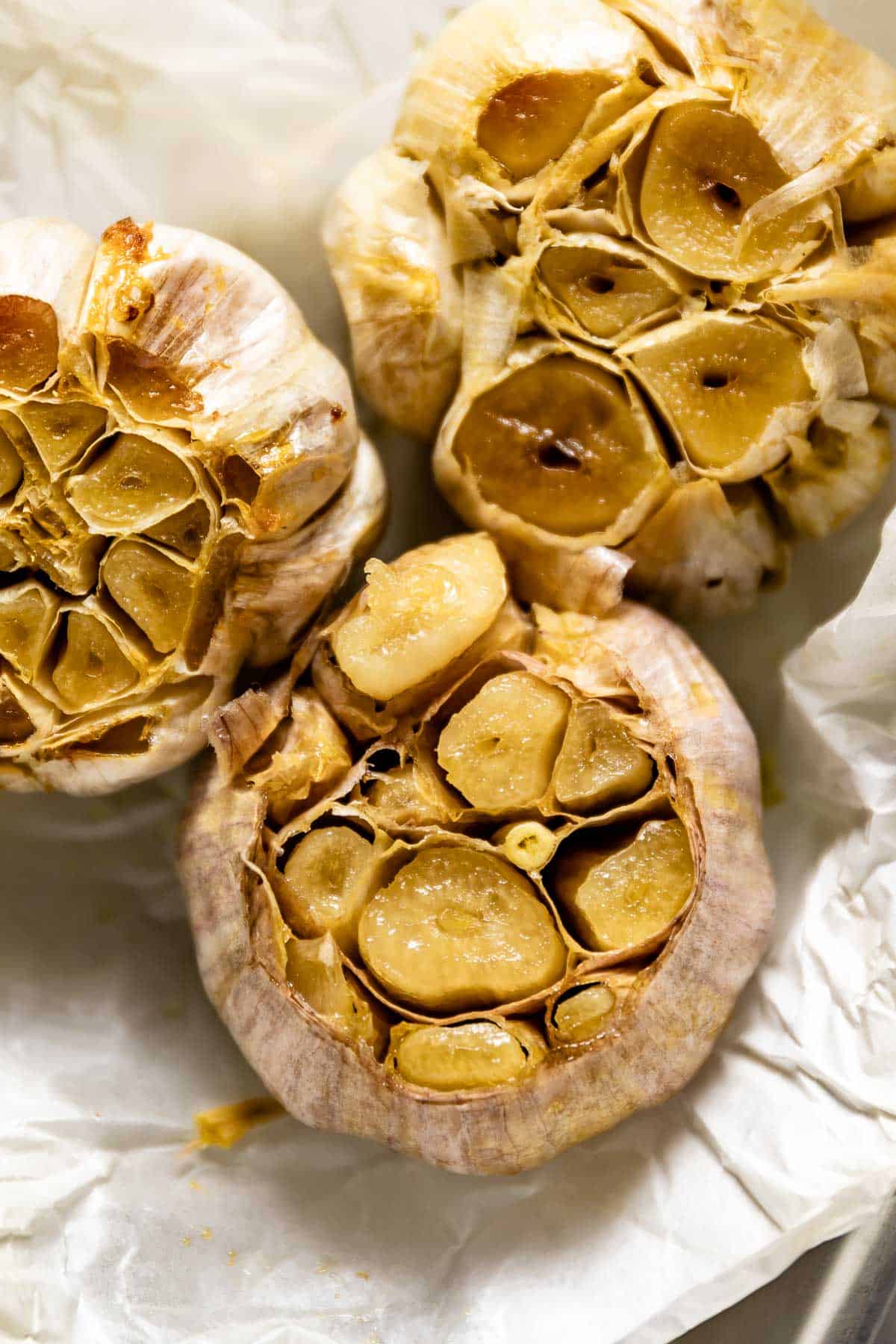 A close-up of roasted heads of garlic on parchment paper from the top view. 