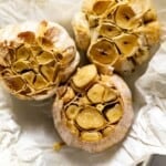 Heads of roasted garlic on parchment paper from the top view.