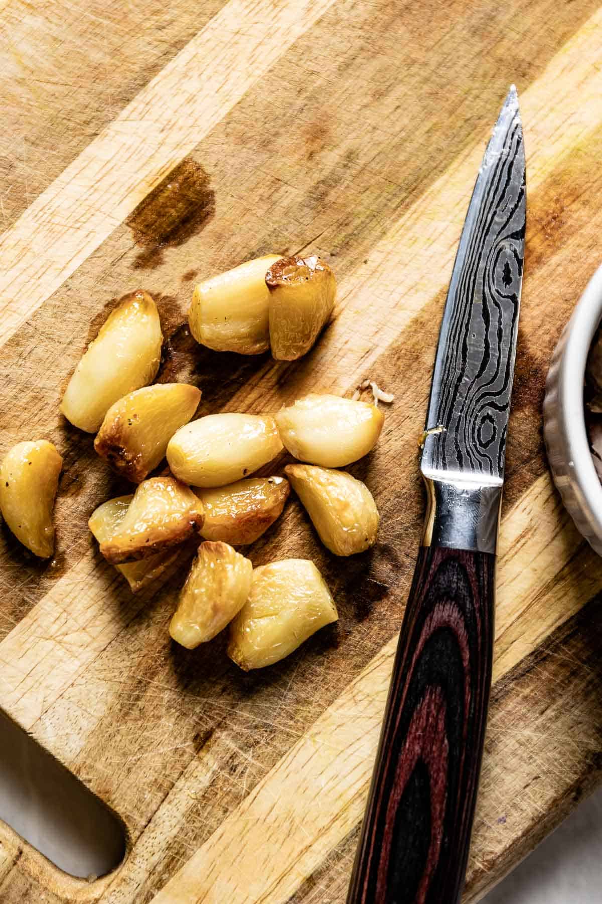 Cloves of roasted garlic on a cutting board with a knife from the top view. 