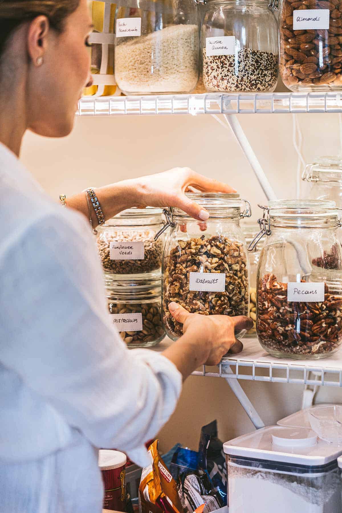 A woman is putting a jar of nuts in the pantry.