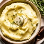 Potatoes mashed with rosemary and butter in a bowl from the top view.