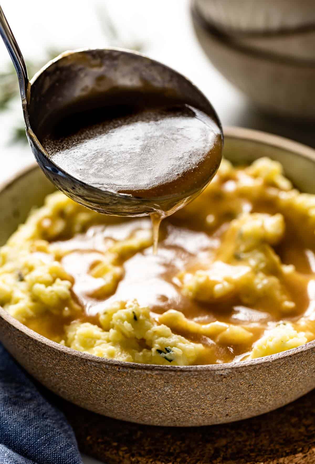 A person ladling gravy over mashed potatoes from the side view.