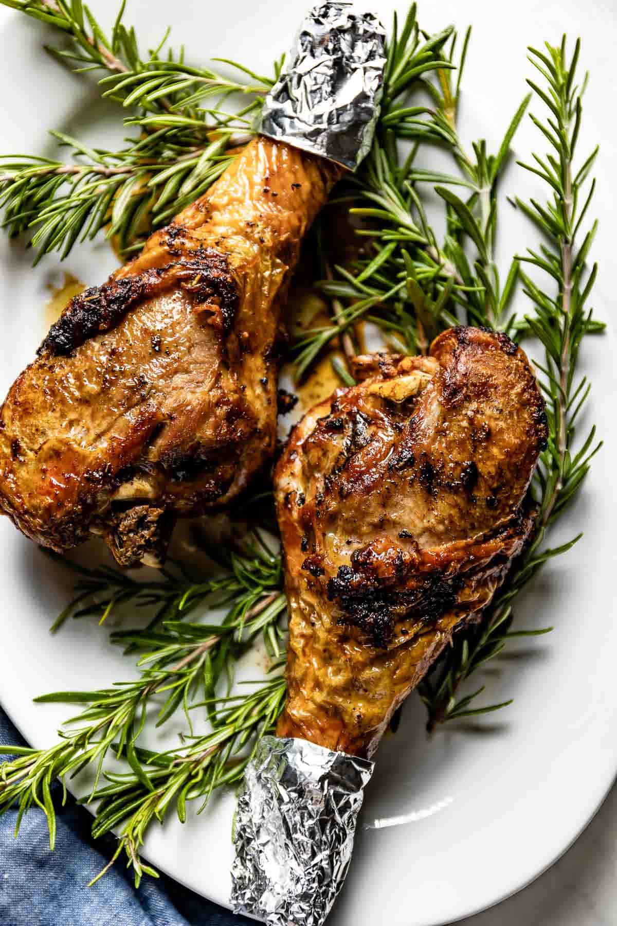 Crispy roasted turkey legs on a plate with rosemary from the top view. 