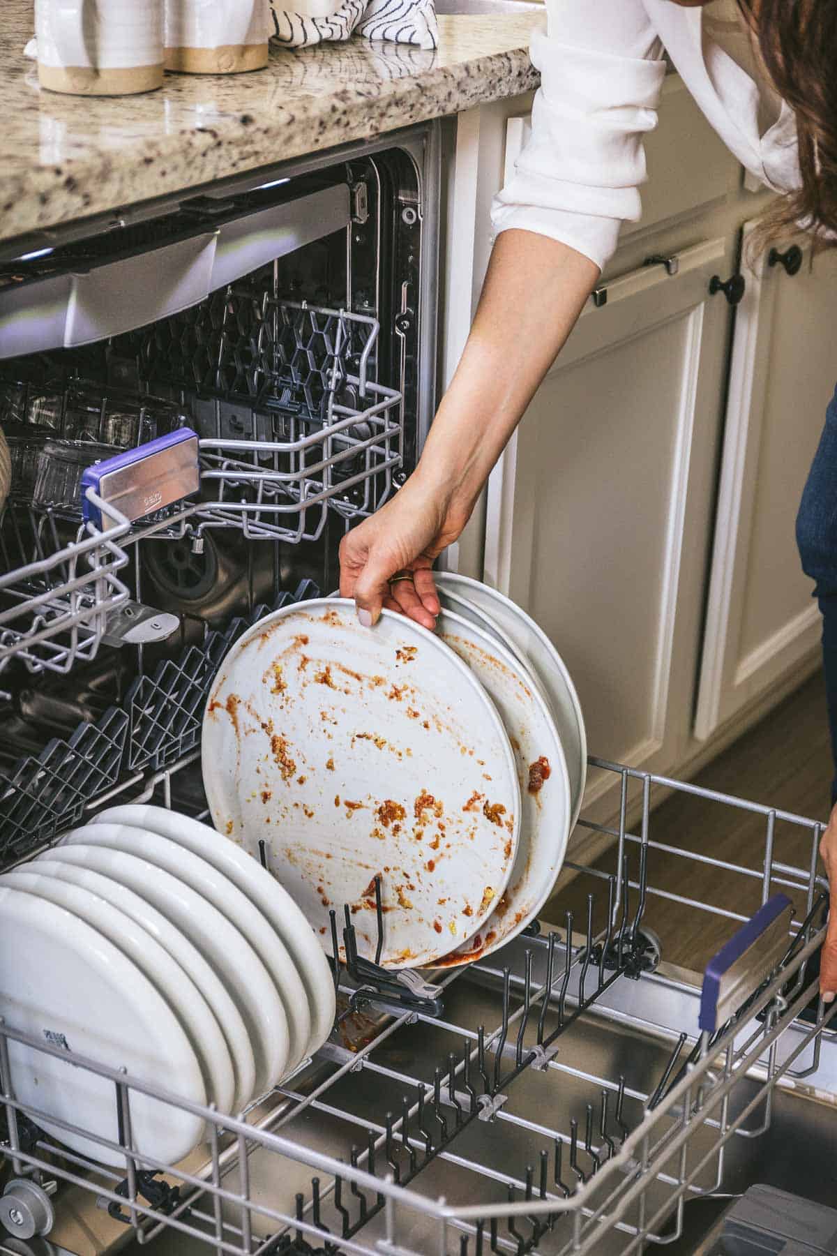 Woman placing a dirty dish in a dishwasher.
