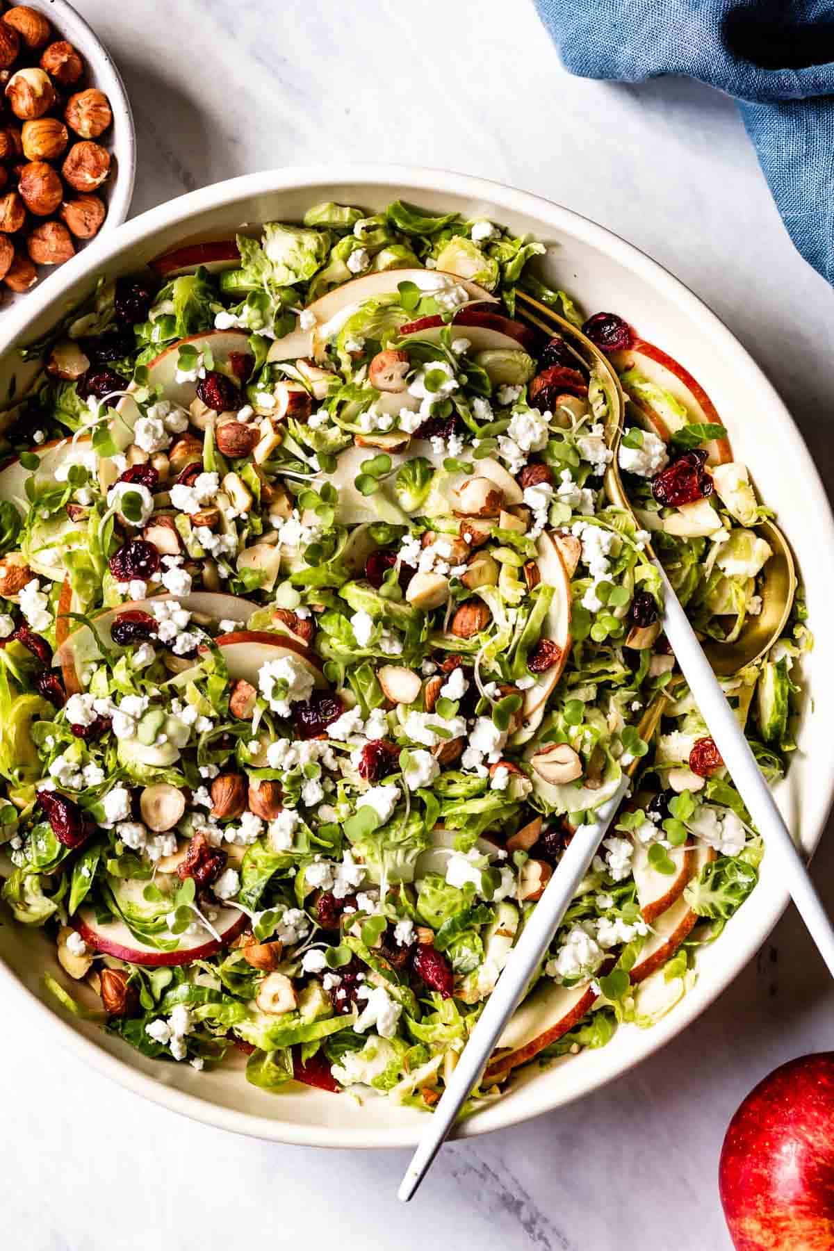 Brussels Sprout Salad in a bowl with an apple on the side.