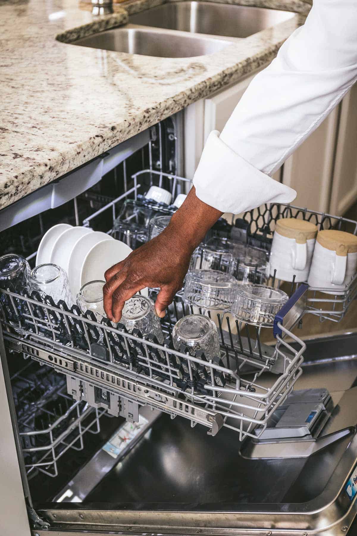 A man placing a glass in the top shelf of a dishwasher.