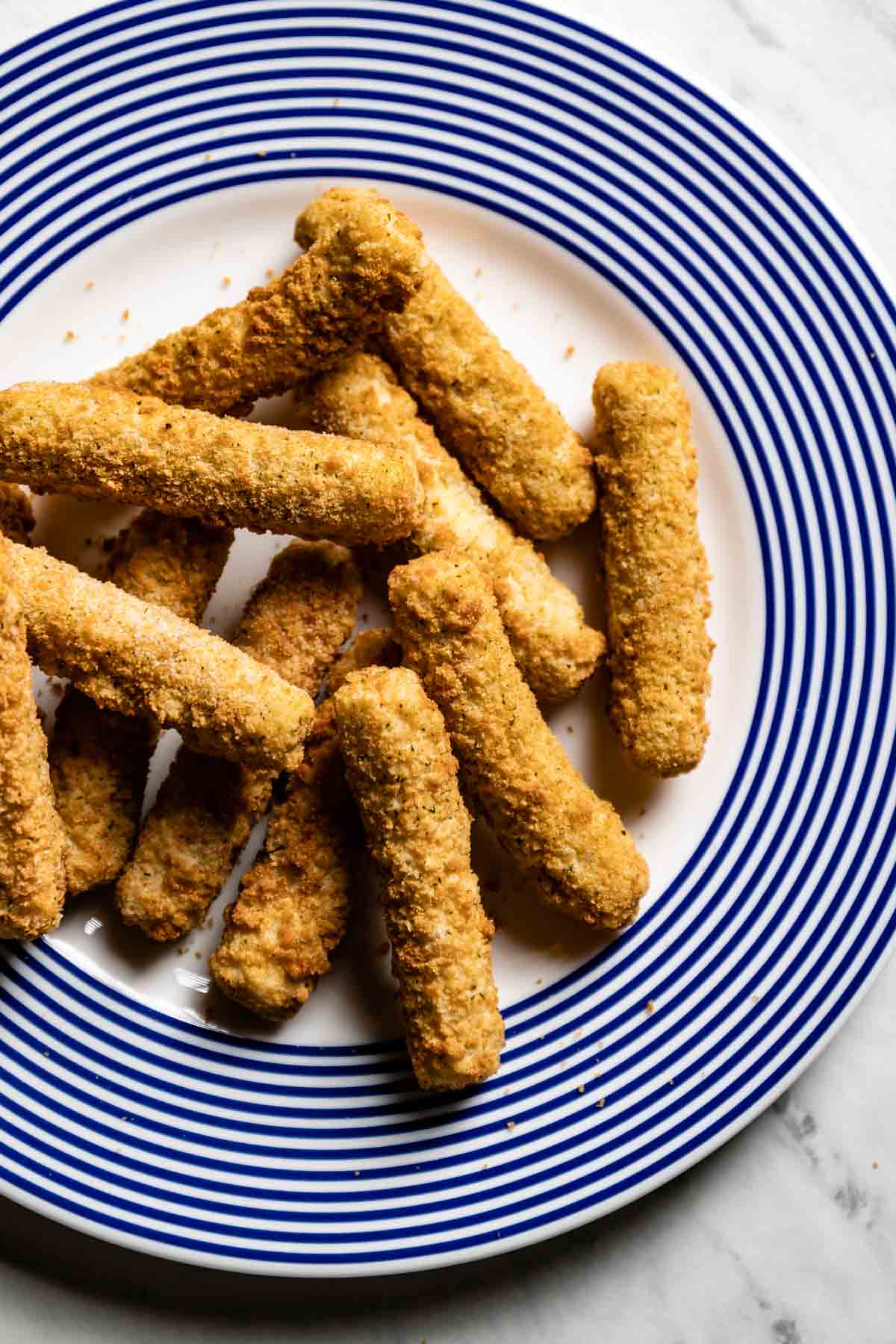 Frozen breaded cheese sticks on a plate from the top view.