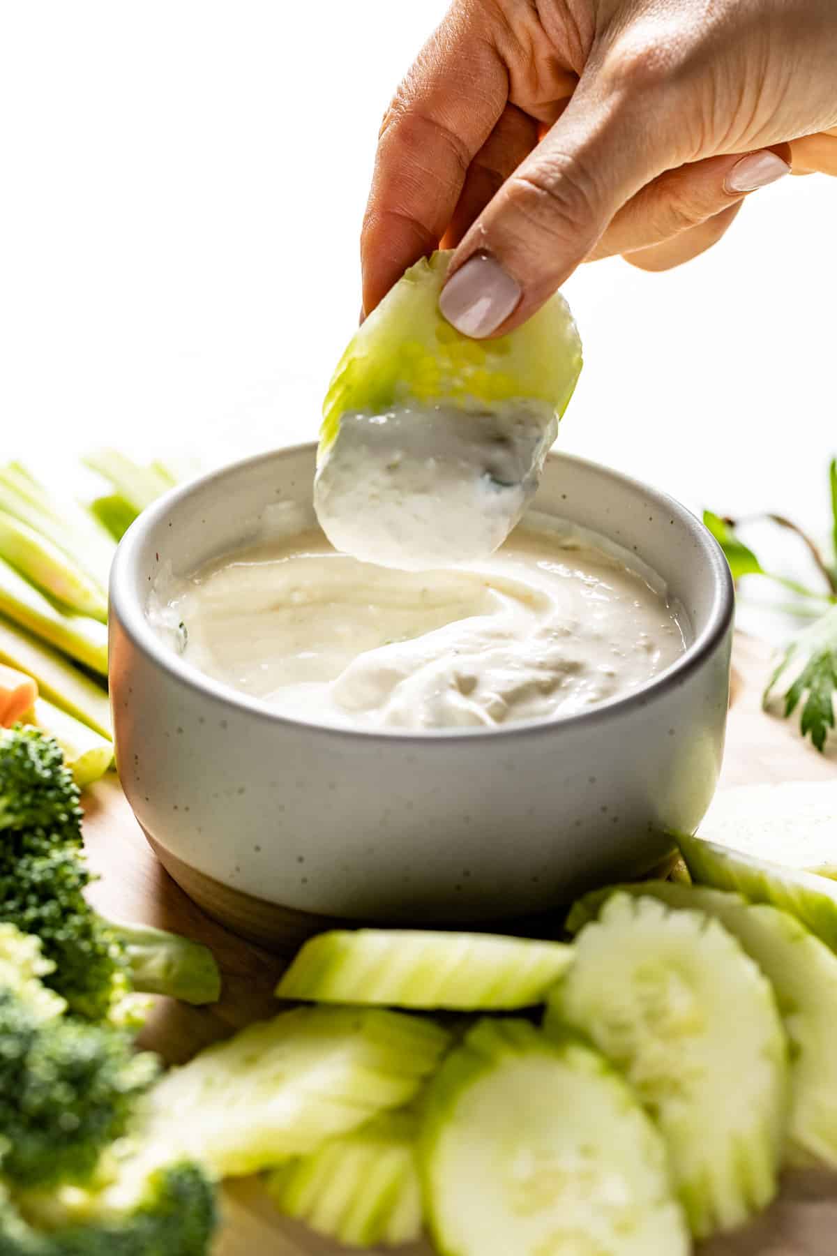 A person dipping a cucumber into a veggie dip from the side view. 