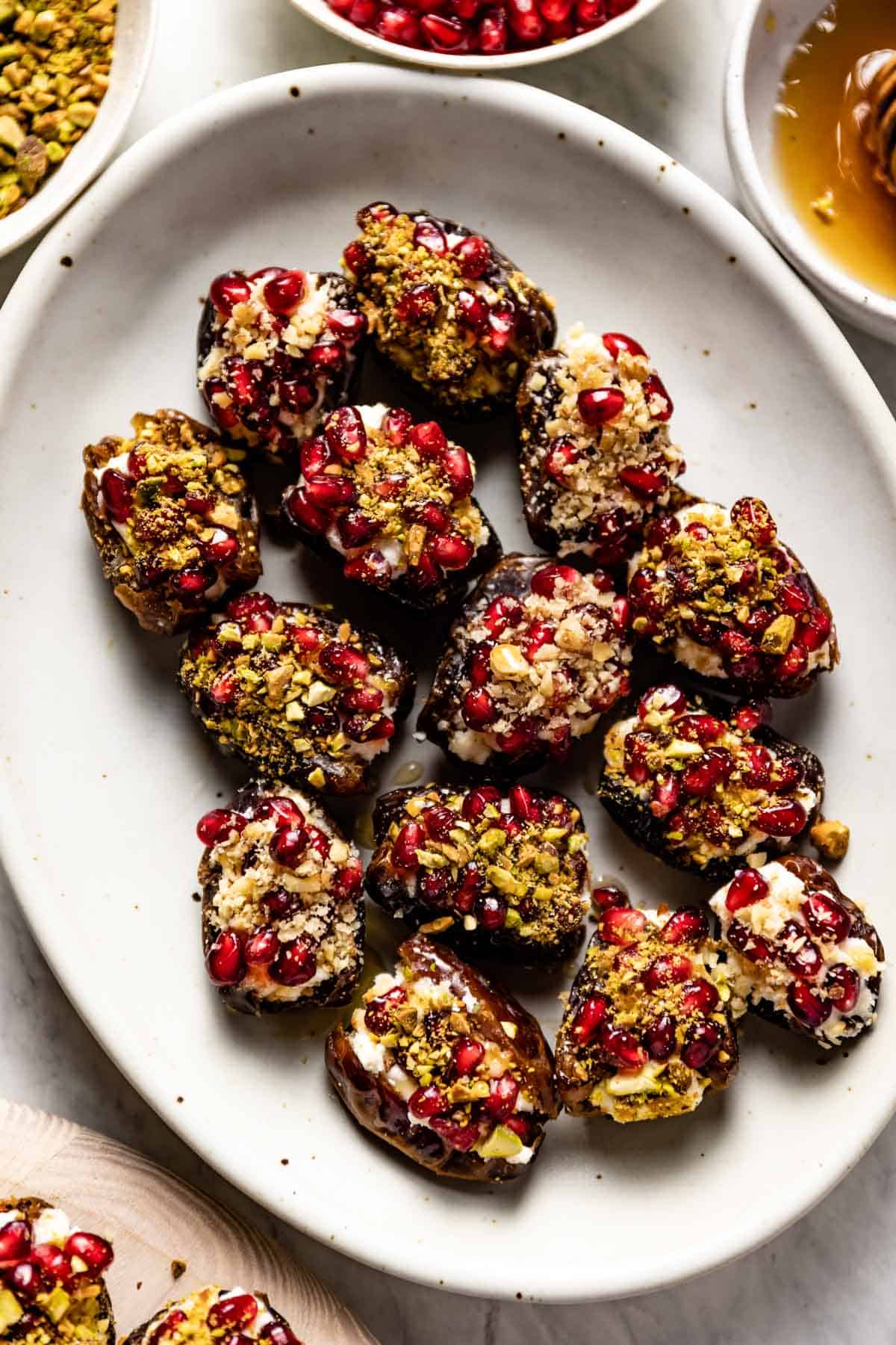 Mascarpone stuffed dates on a plate topped off with pomegranate seeds and nuts. 