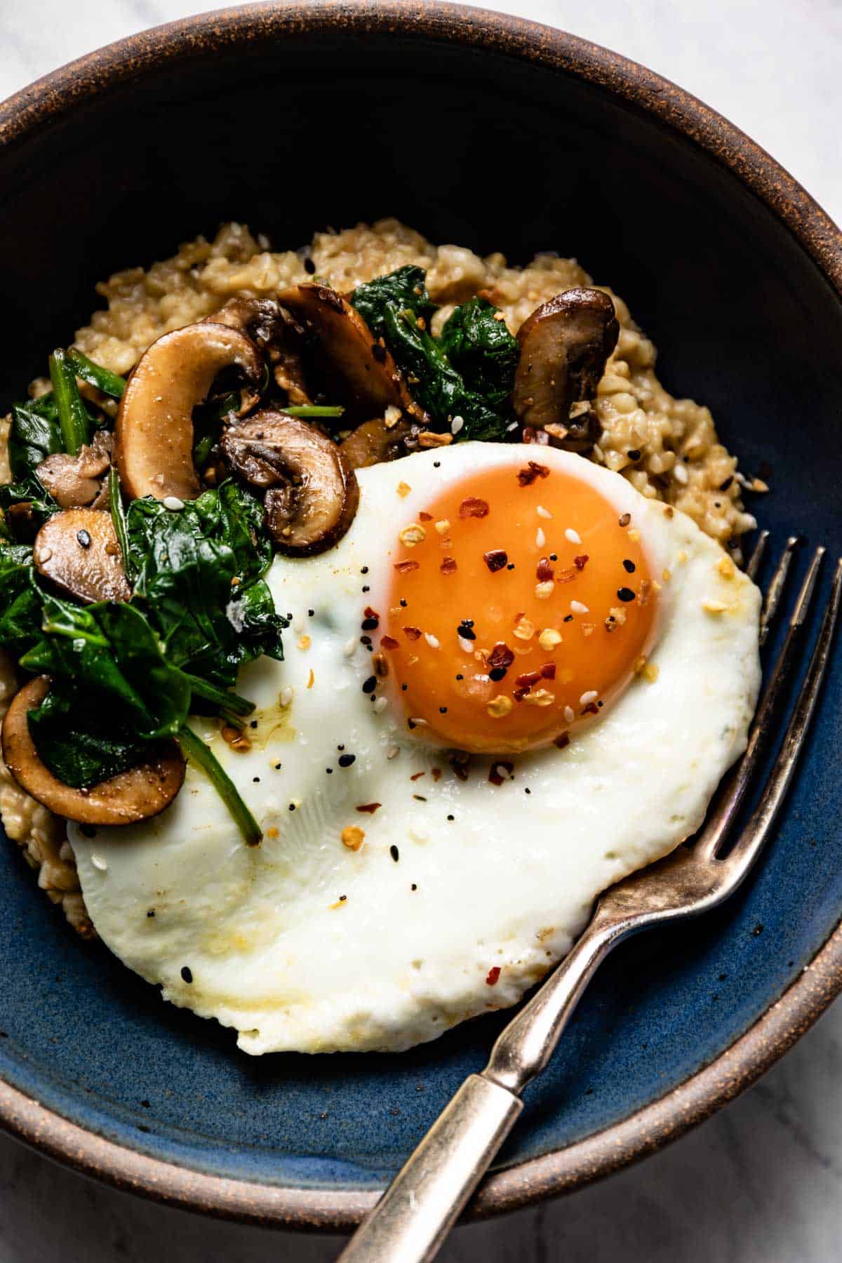 A bowl of oats topped with an egg, mushrooms, and spinach from the top view.