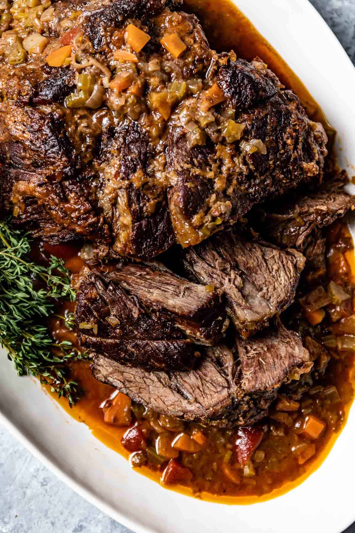 A company pot roast with herbs and veggies on a plate from the top view.