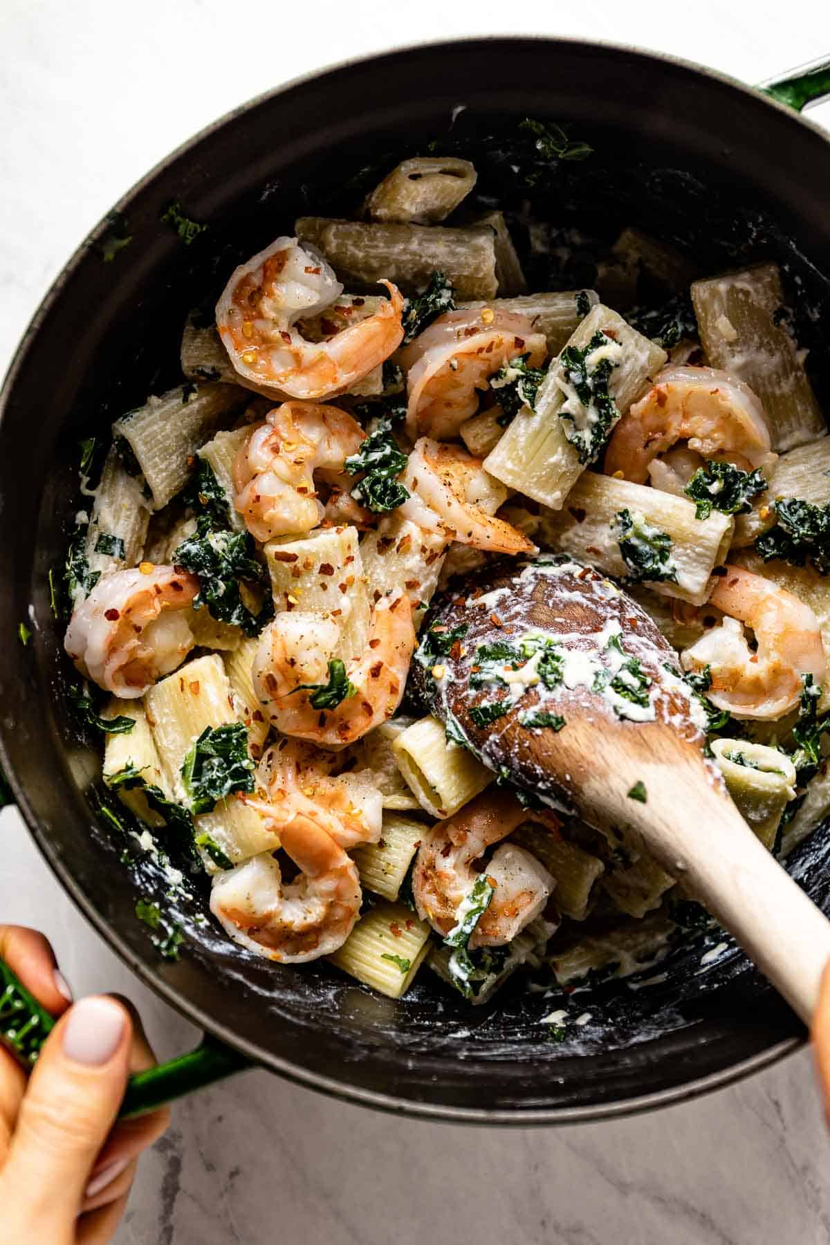 Person mixing lemon ricotta shrimp pasta in a dutch oven with a wooden spoon.