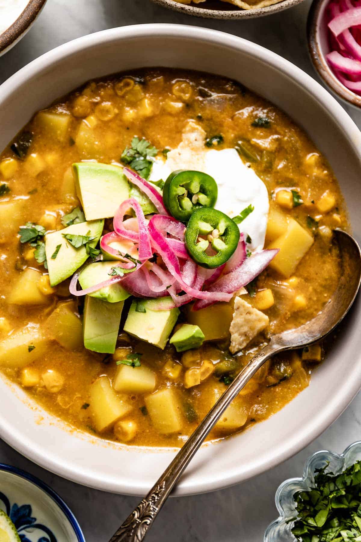 A Mexican-inspired soup with corn in a bowl with a spoon from the top view. 