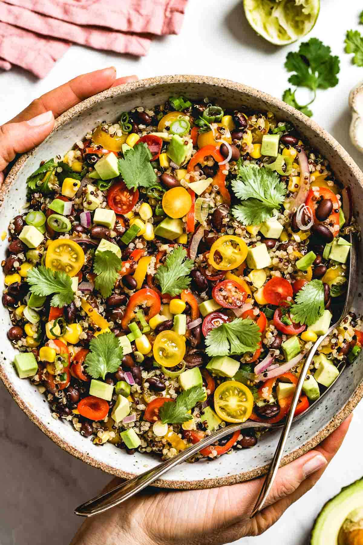 A big bowl of Southwest Quinoa Salad is photographed from the top view as a woman is placing it on the table.