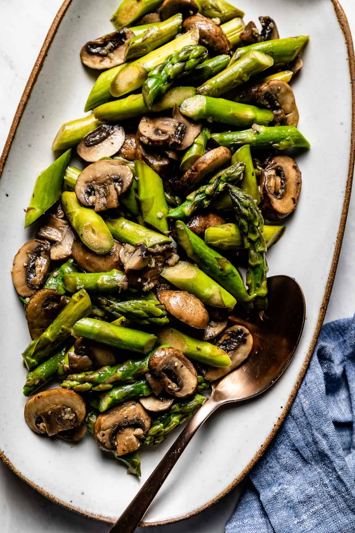 Asparagus and mushroom saute in a plate with a spoon on the side.