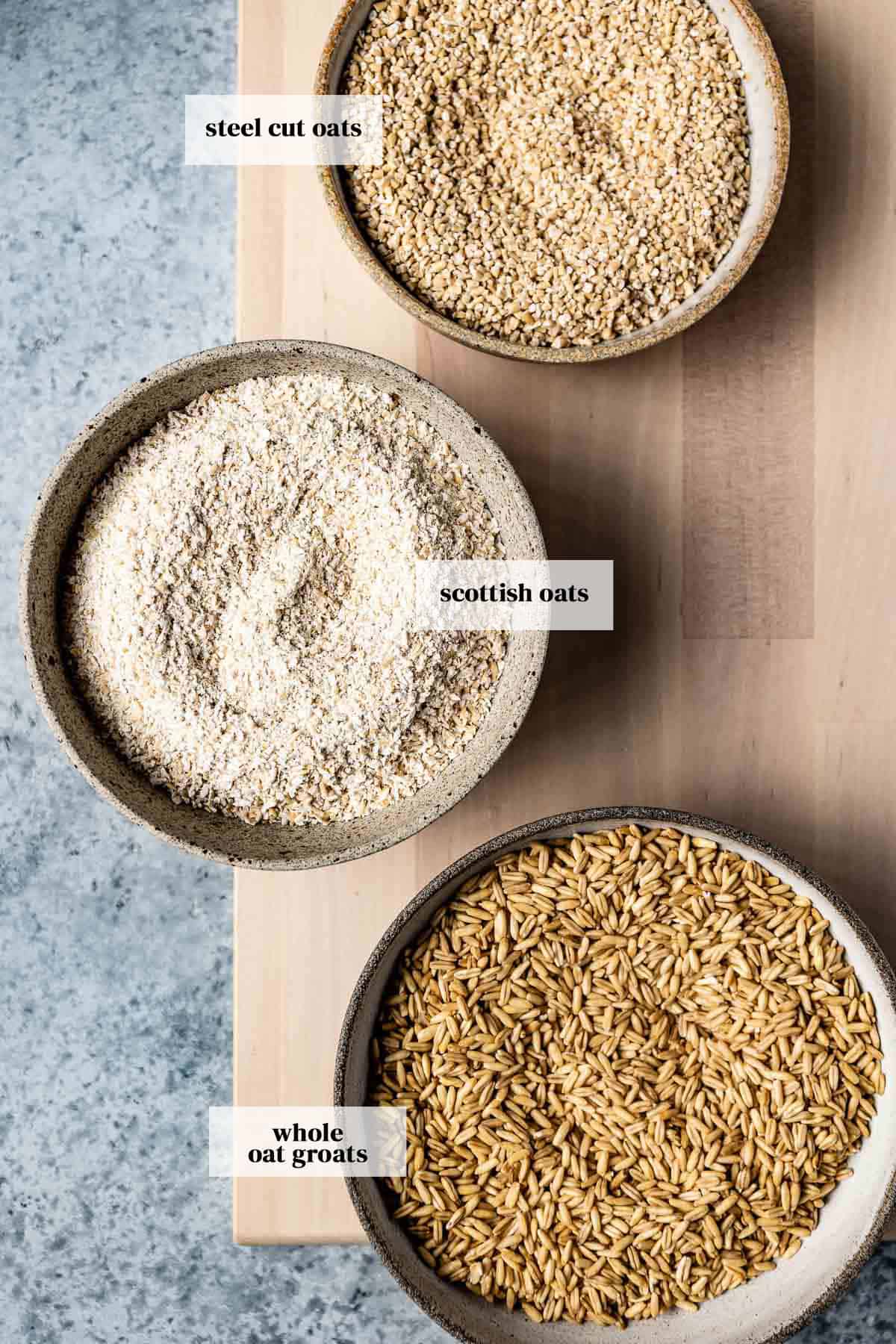 Different kinds of oats (steel cut oats, Scottish oats, and Whole oat groats) are in bowls from the top view.
