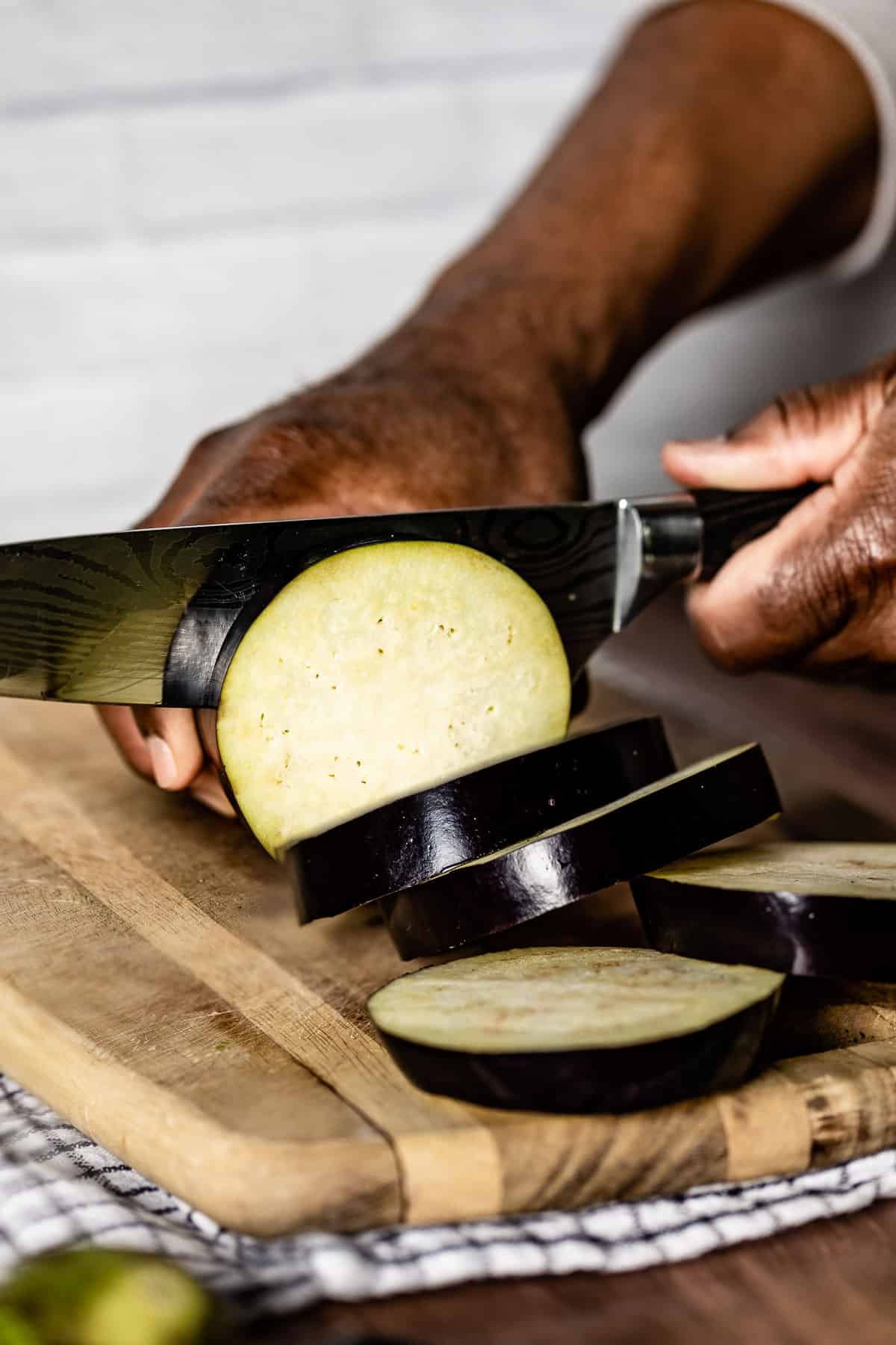 A person cutting an eggplant into rounds shown from the side view.