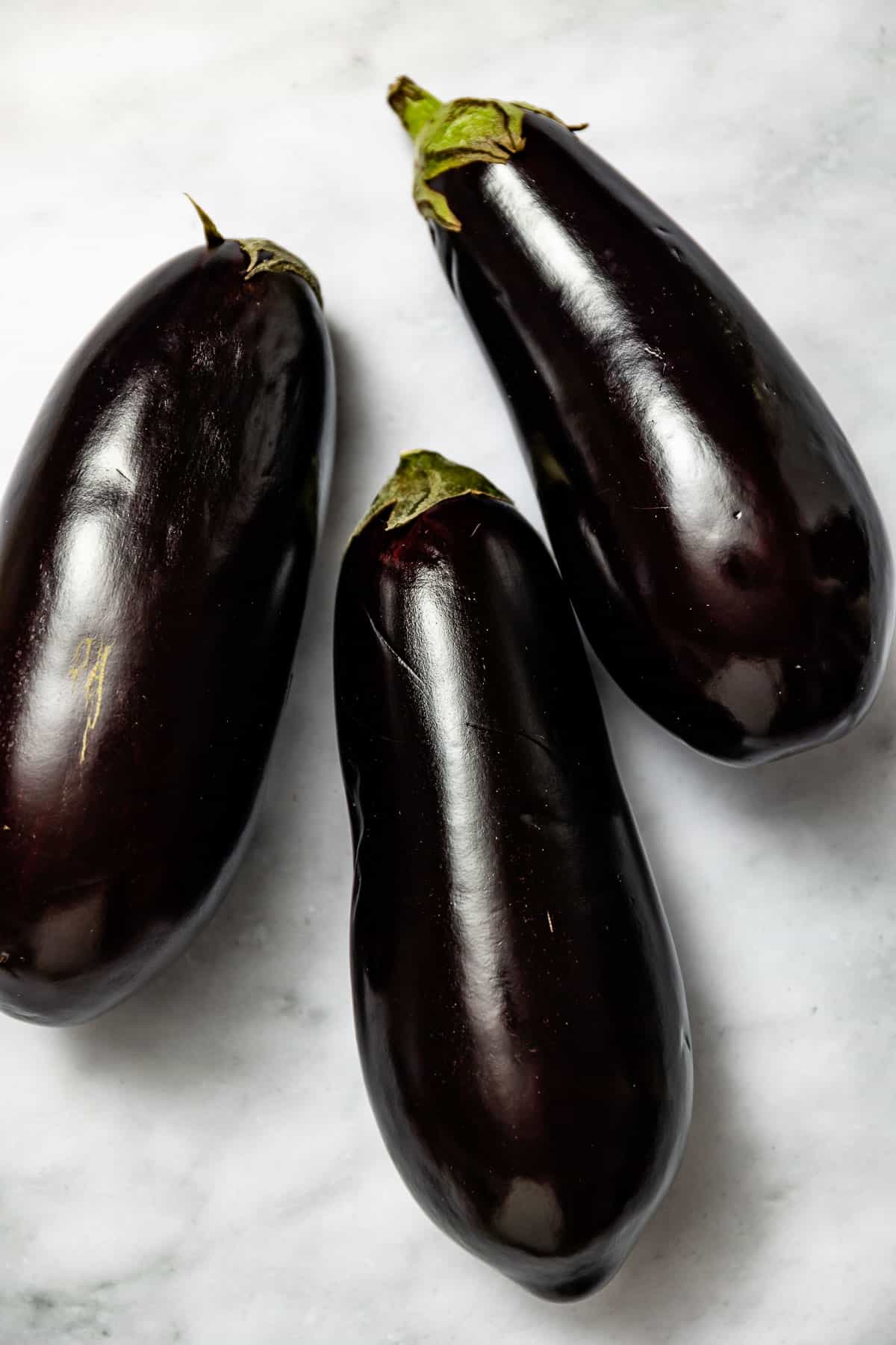 Two globe eggplants next to each other on a white backdrop.