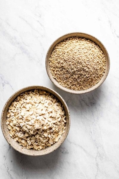 steel cut oats and rolled oats in small bowls on a marble backdrop.