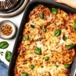 Hands holding a dish of baked eggplant parmesan topped with melted cheese and fresh basil with Pinterest style text on top.