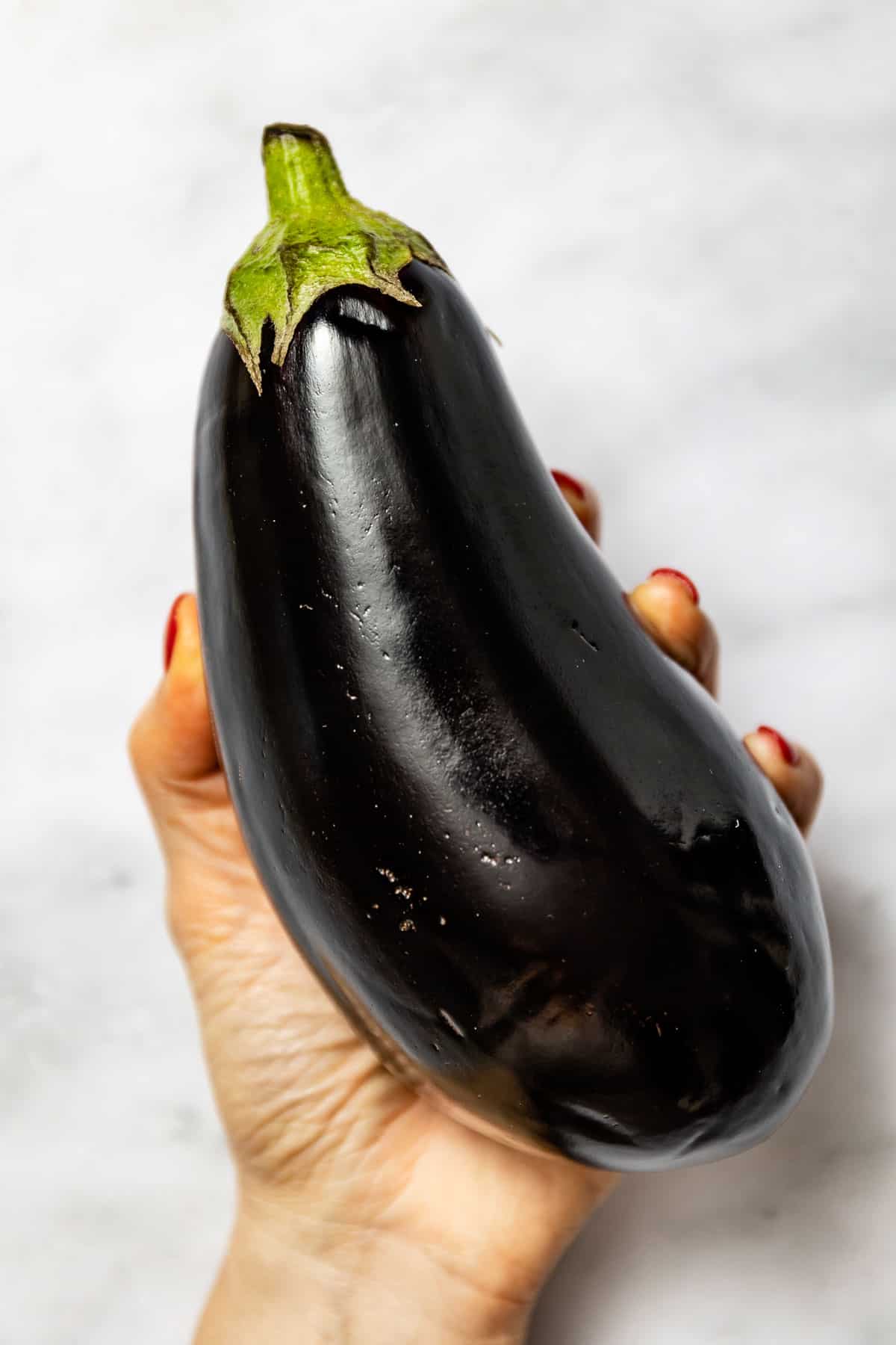An Italian eggplant in the hands of a woman from the top view.