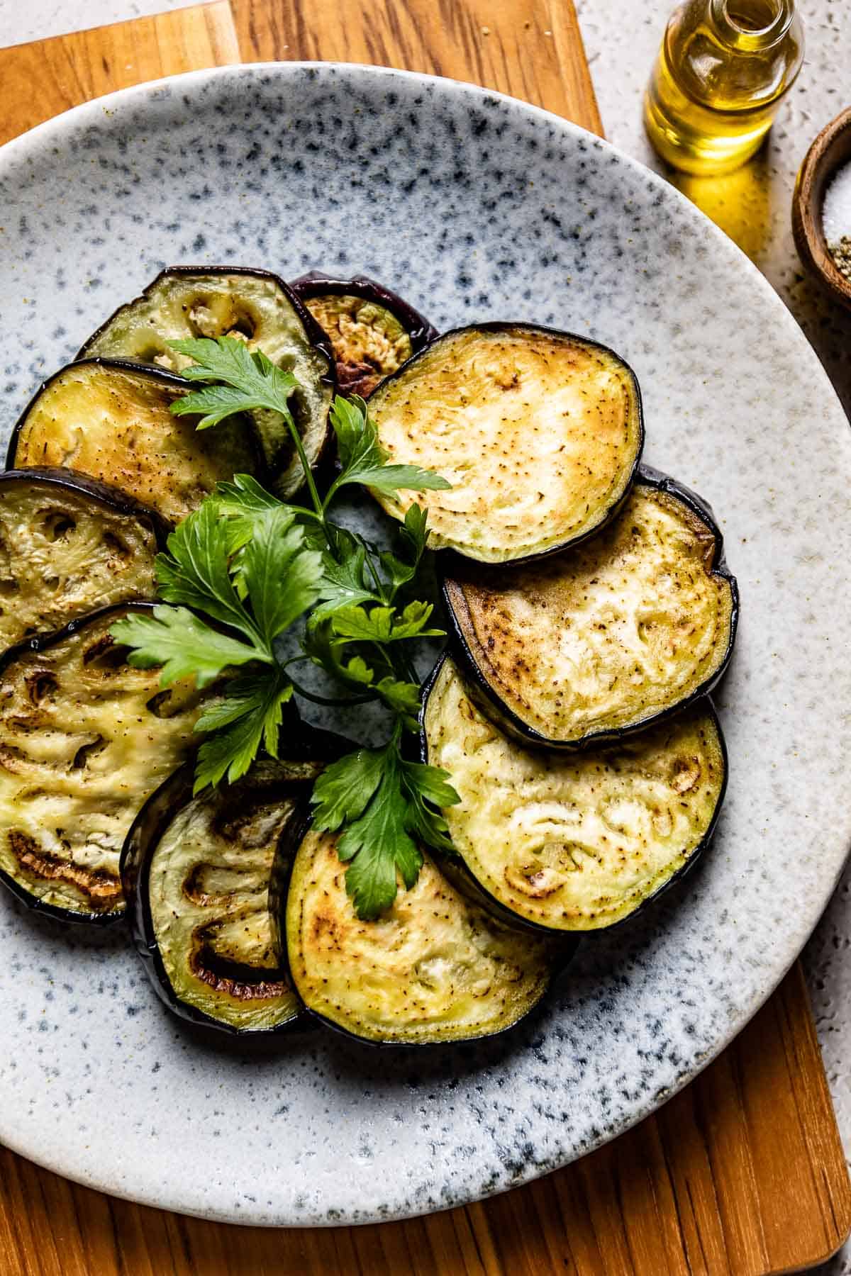 Sauteed eggplant slices on a plate garnished with fresh parsley.