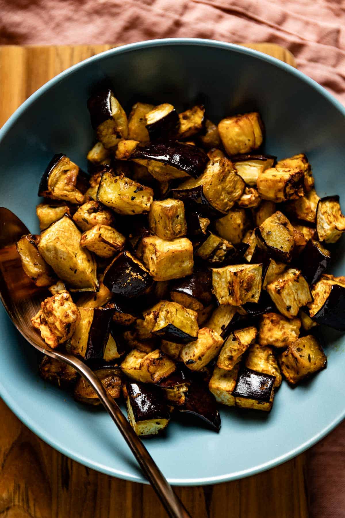 Air fried eggplant cubes placed in a bowl with a spoon on the side.