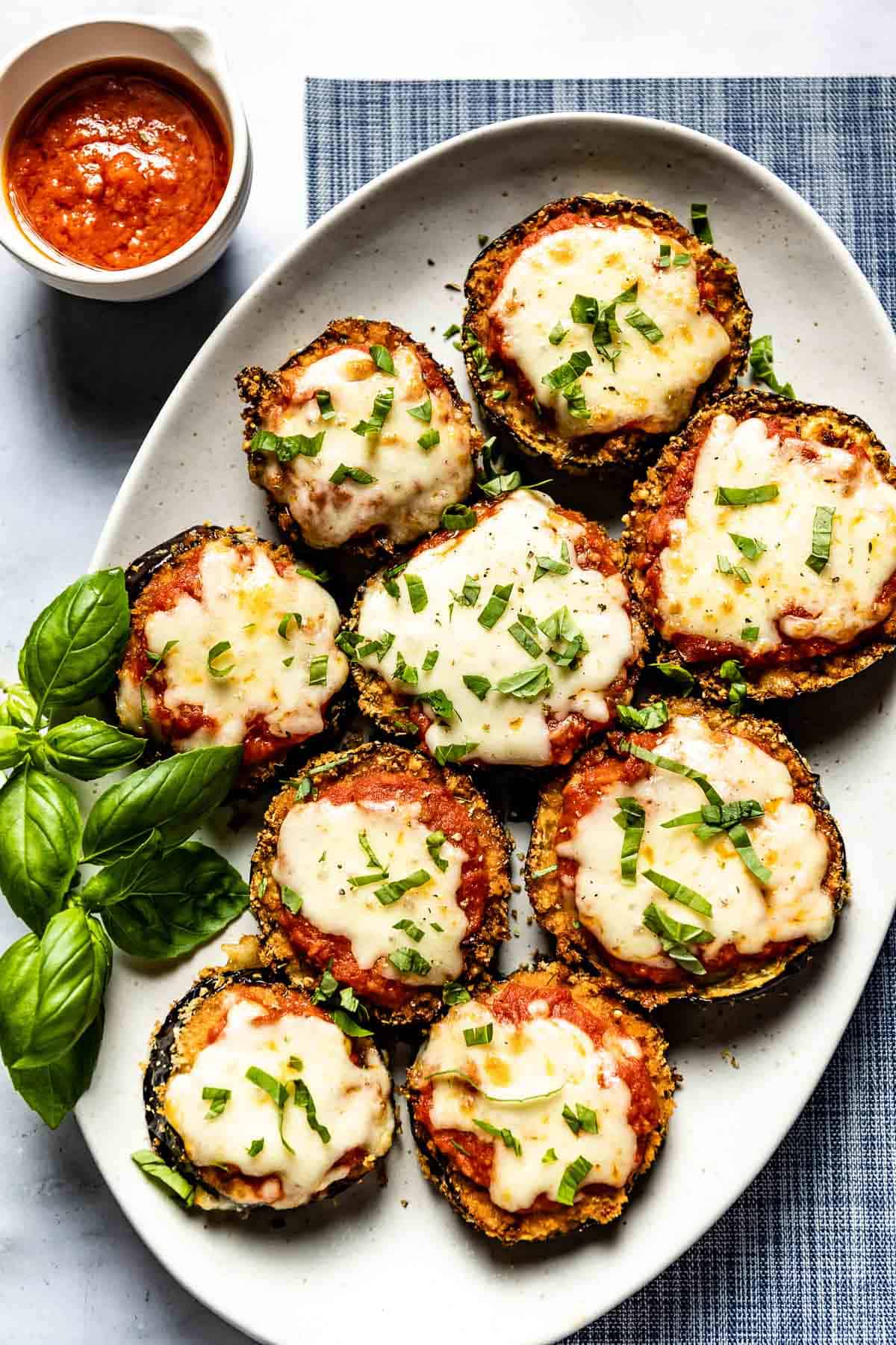 Air fried eggplant parmesan garnished with fresh basil on an oval plate.