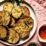 Air fry breaded eggplant slices on a plate with marinara sauce for dippigng on the side.