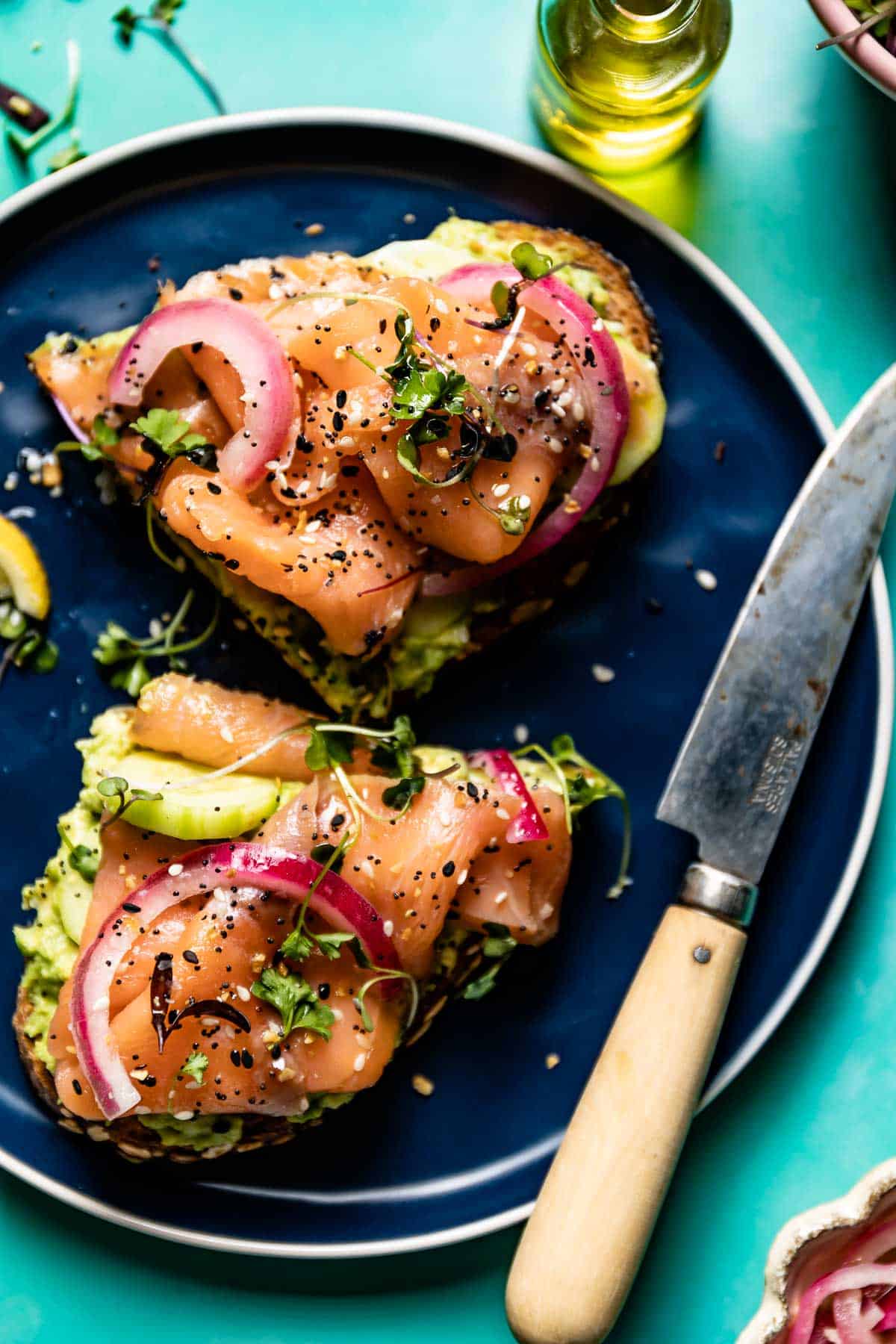 Smoked Salmon Avocado Toast cut in half on a plate with a knife on the side.