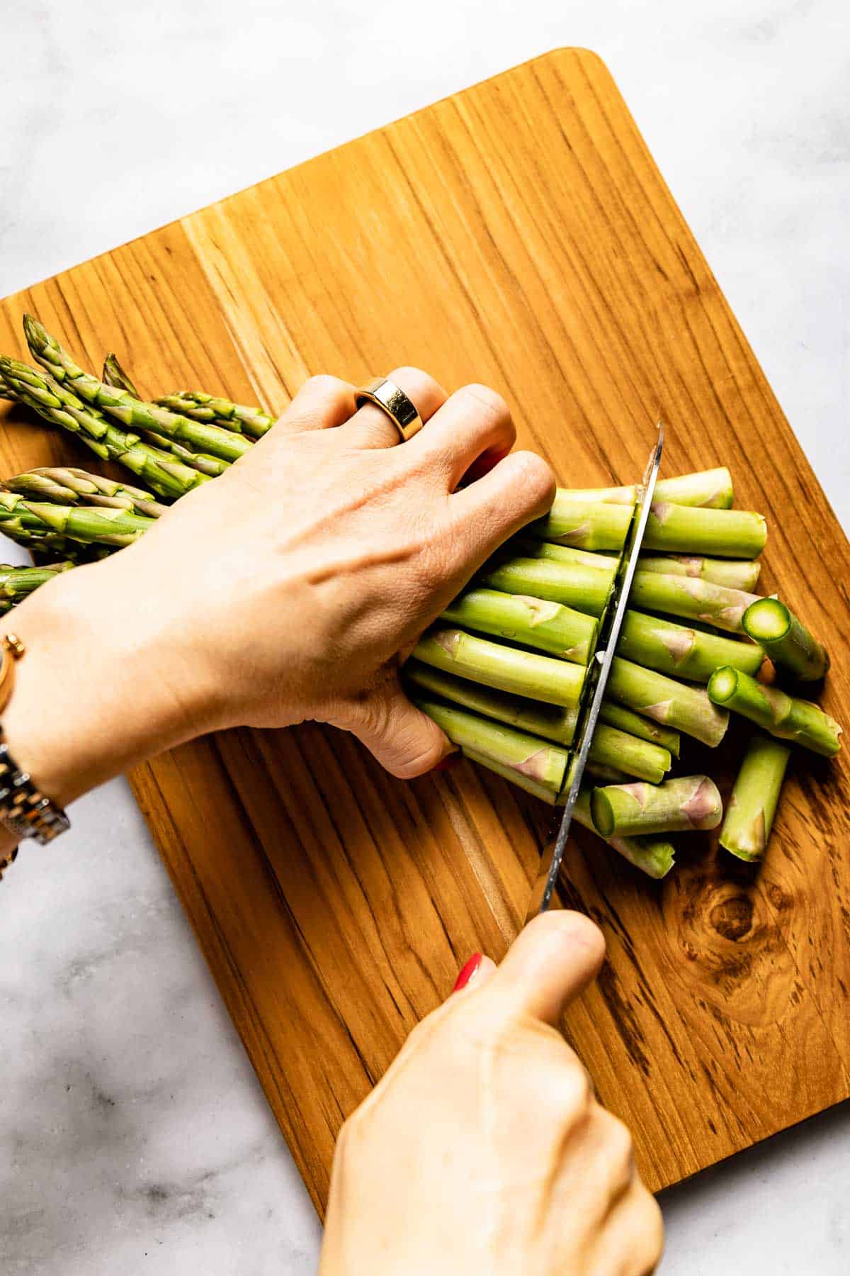 Person cutting the woody ends of asparagus on a cutting board.