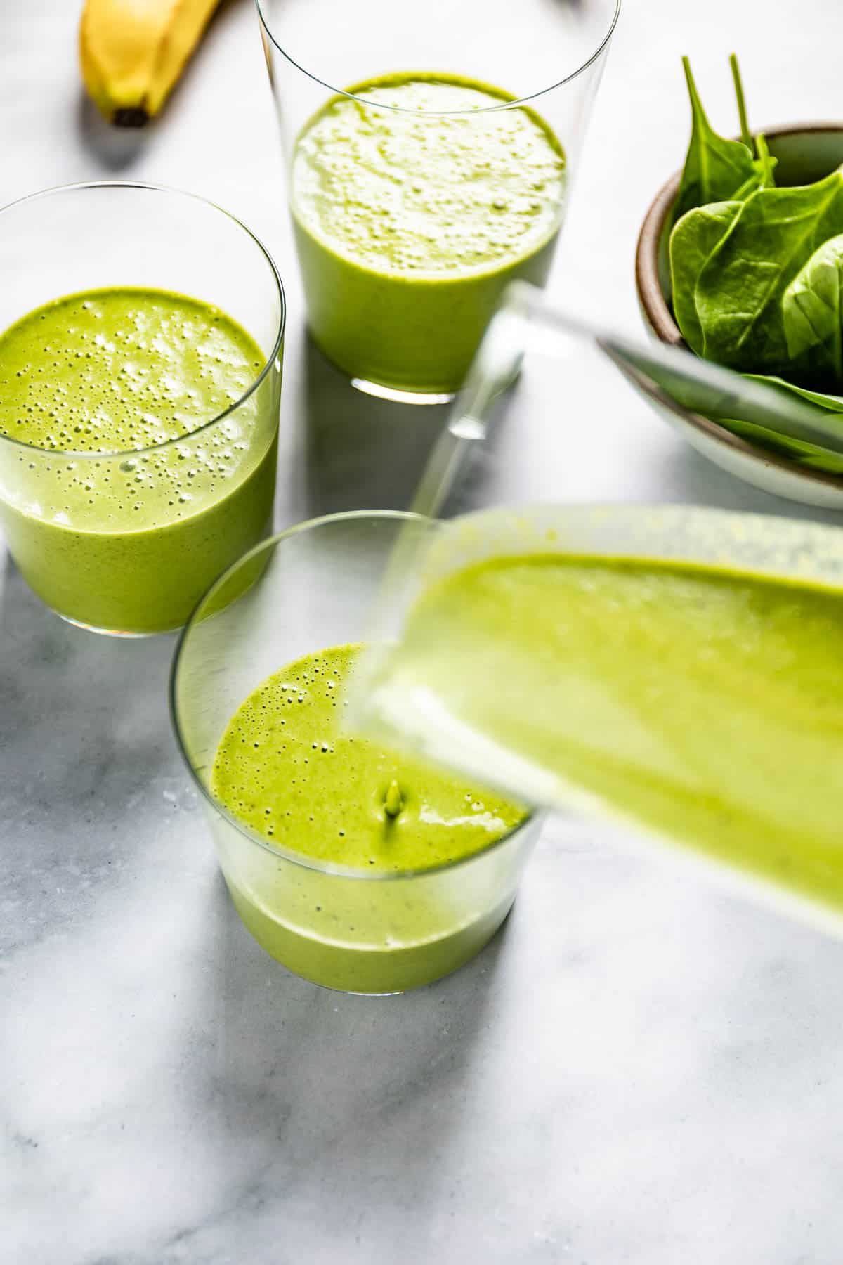 A person pouring smoothie with spinach and banana in a glass.