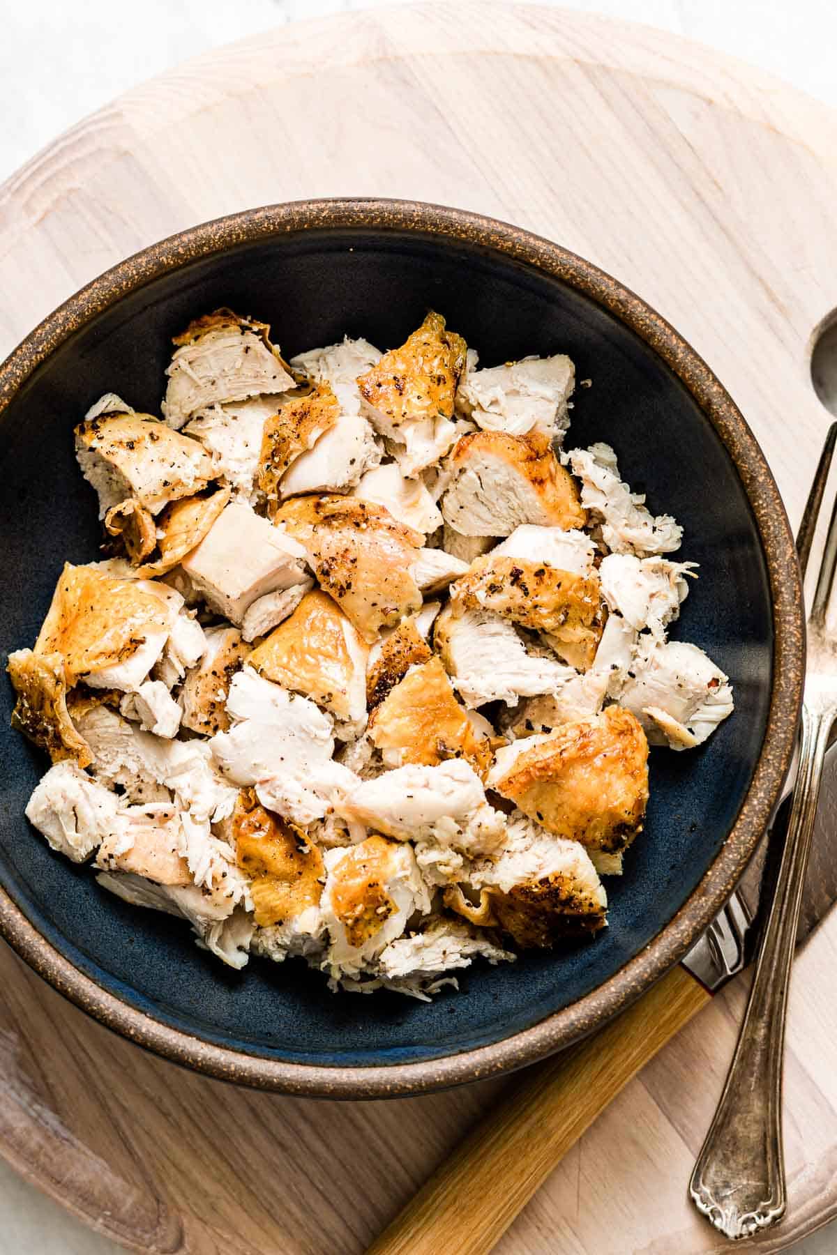 A bowl of sliced oven baked bone in chicken with a fork and knife on the side.