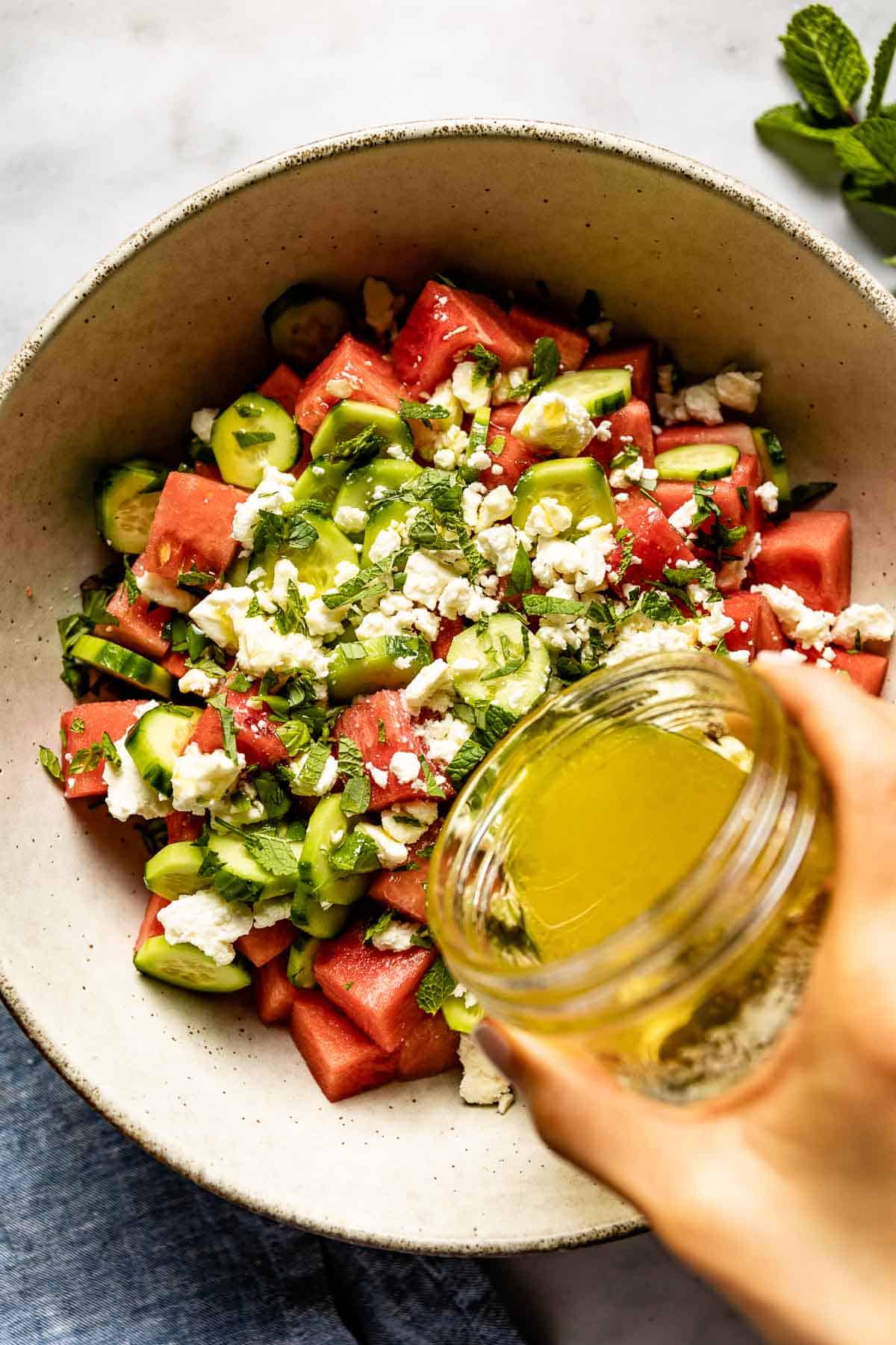 Person drizzling a watermelon salad with honey lime dressing from the top view.