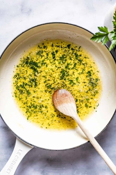 Garlic butter sauce garnished with parsley in a skillet with a wooden spoon.