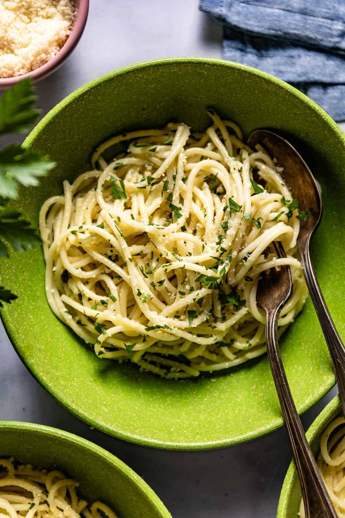 Buttered pasta in a bowl garnished with parsley and parmesan cheese.